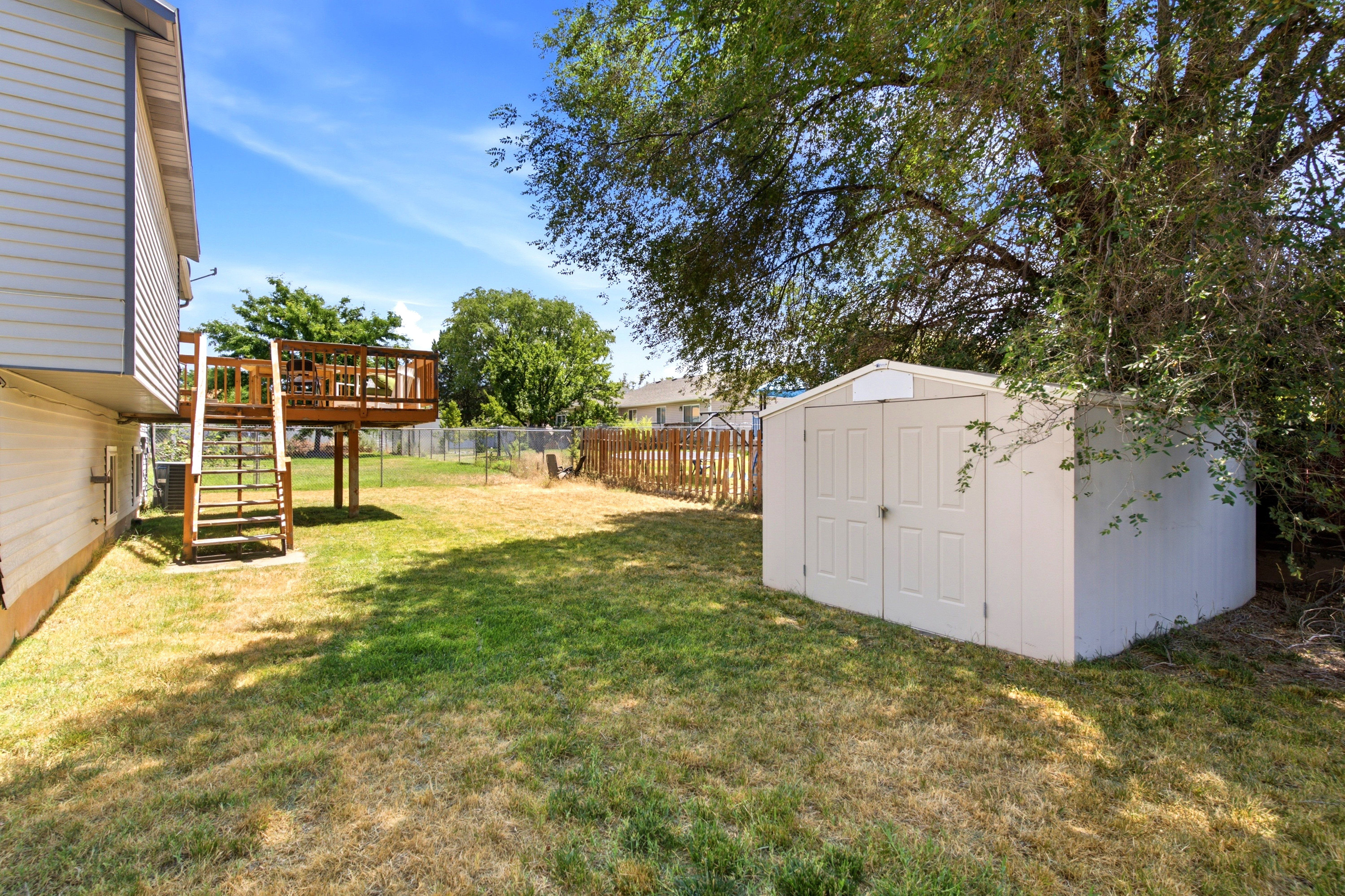 Expansive backyard featuring a raised wooden deck with railings, a storage shed, and mature trees