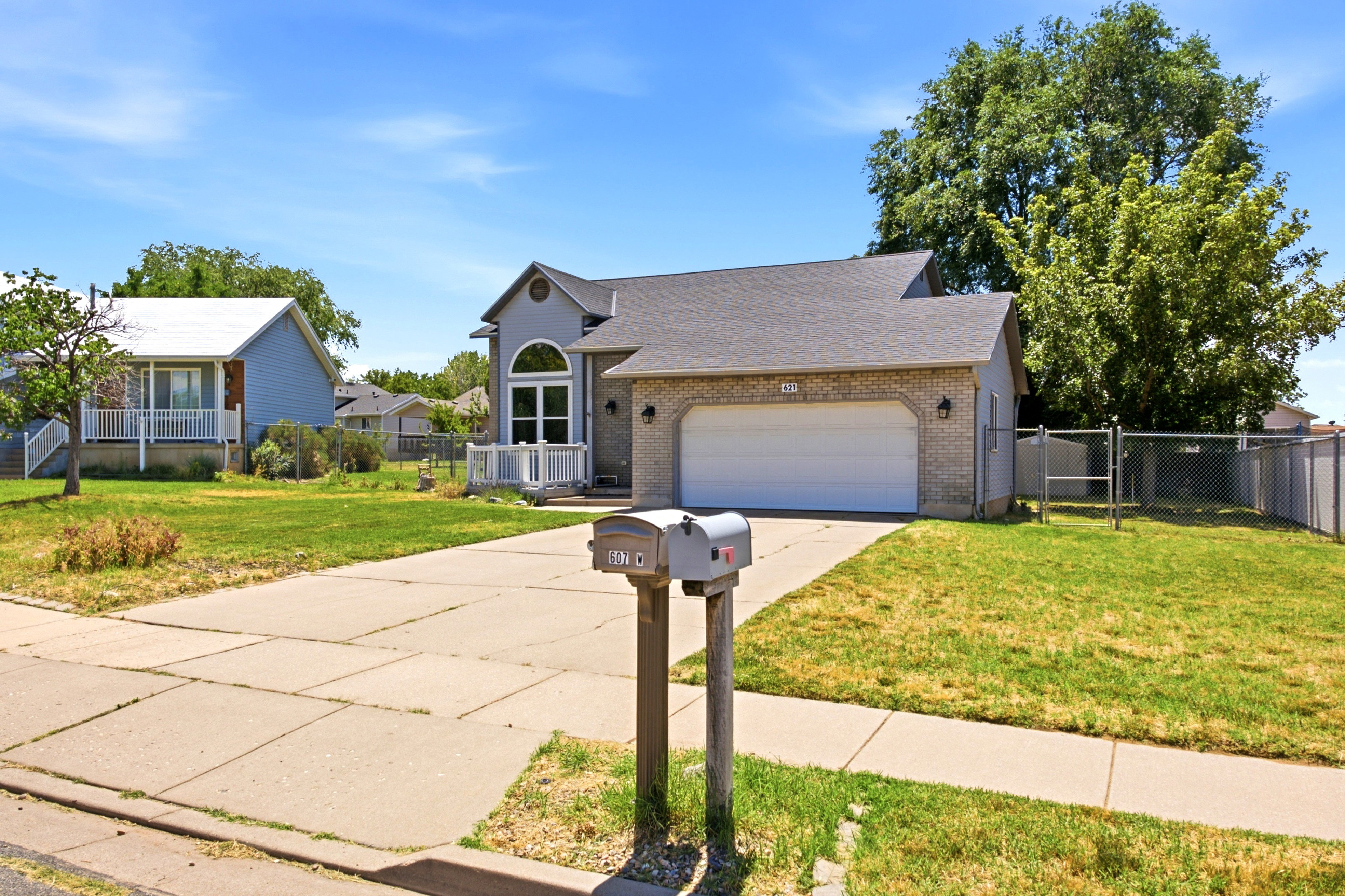 Contemporary-style residence featuring a two-car garage with an arched window above, brick and siding exterior, and a fenced side yard