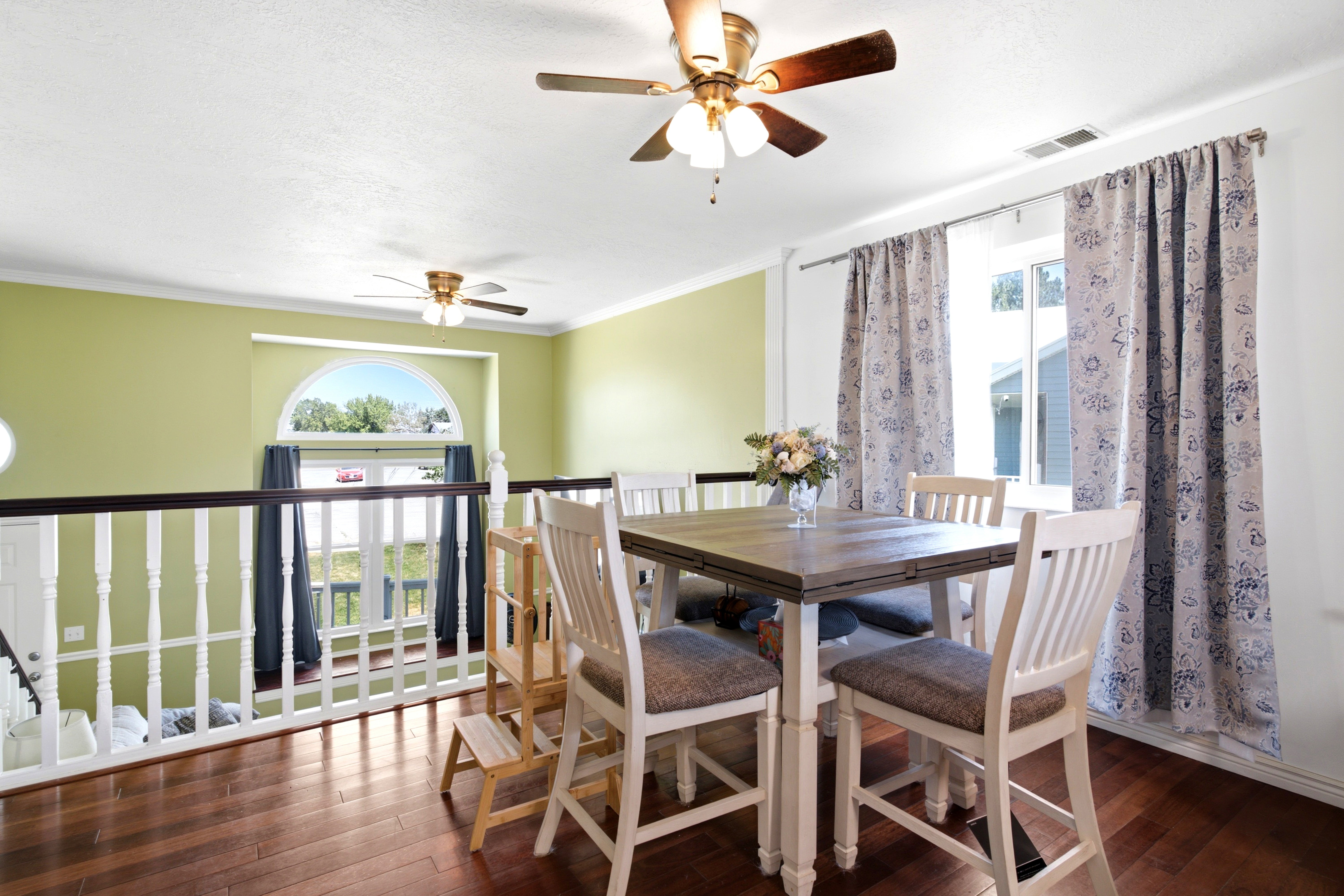 Hardwood-finish flooring featuring a white balustrade railing and a light green accent wall