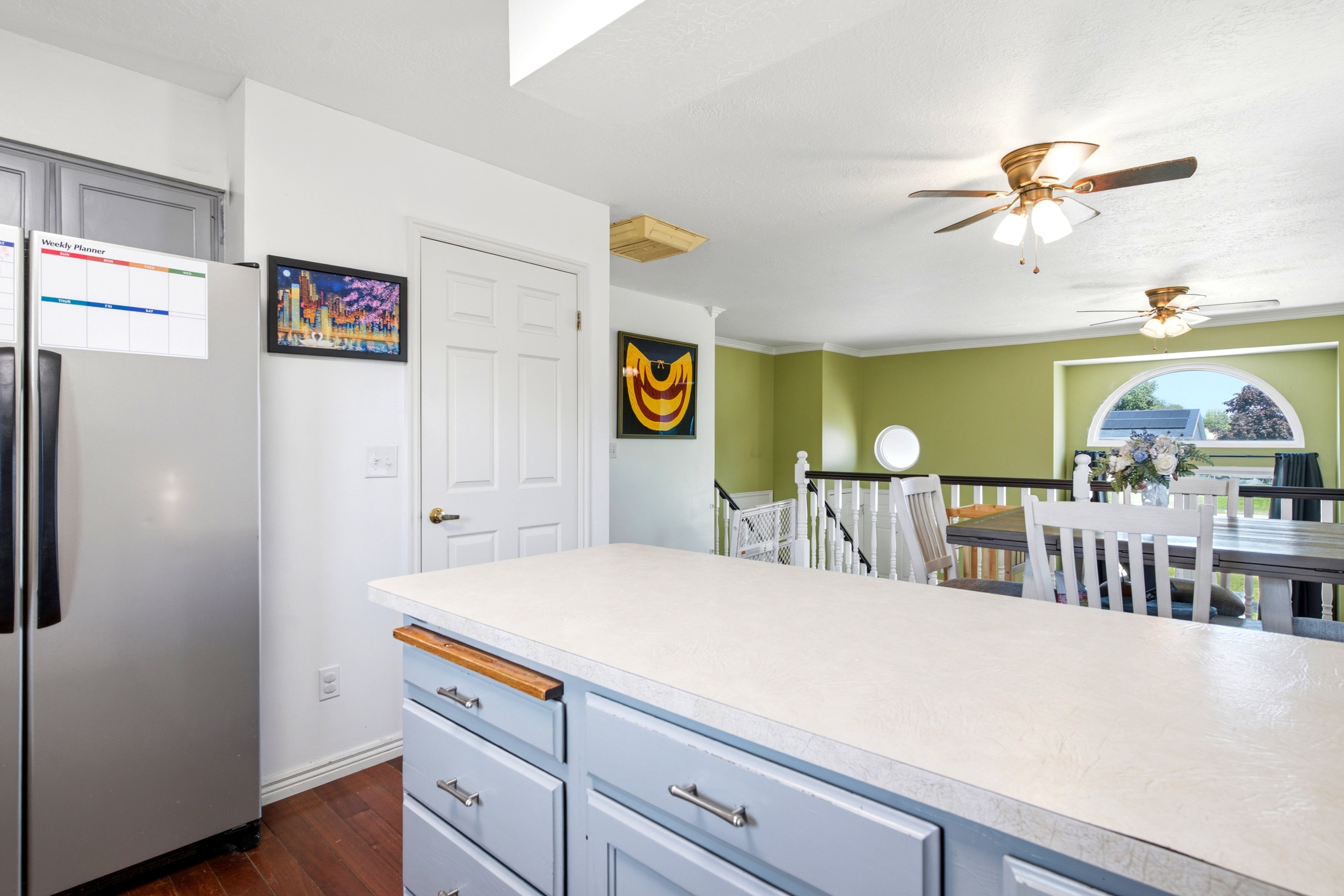Kitchen island featuring light-toned countertop, light blue cabinetry with brushed nickel hardware, and wood-finish flooring