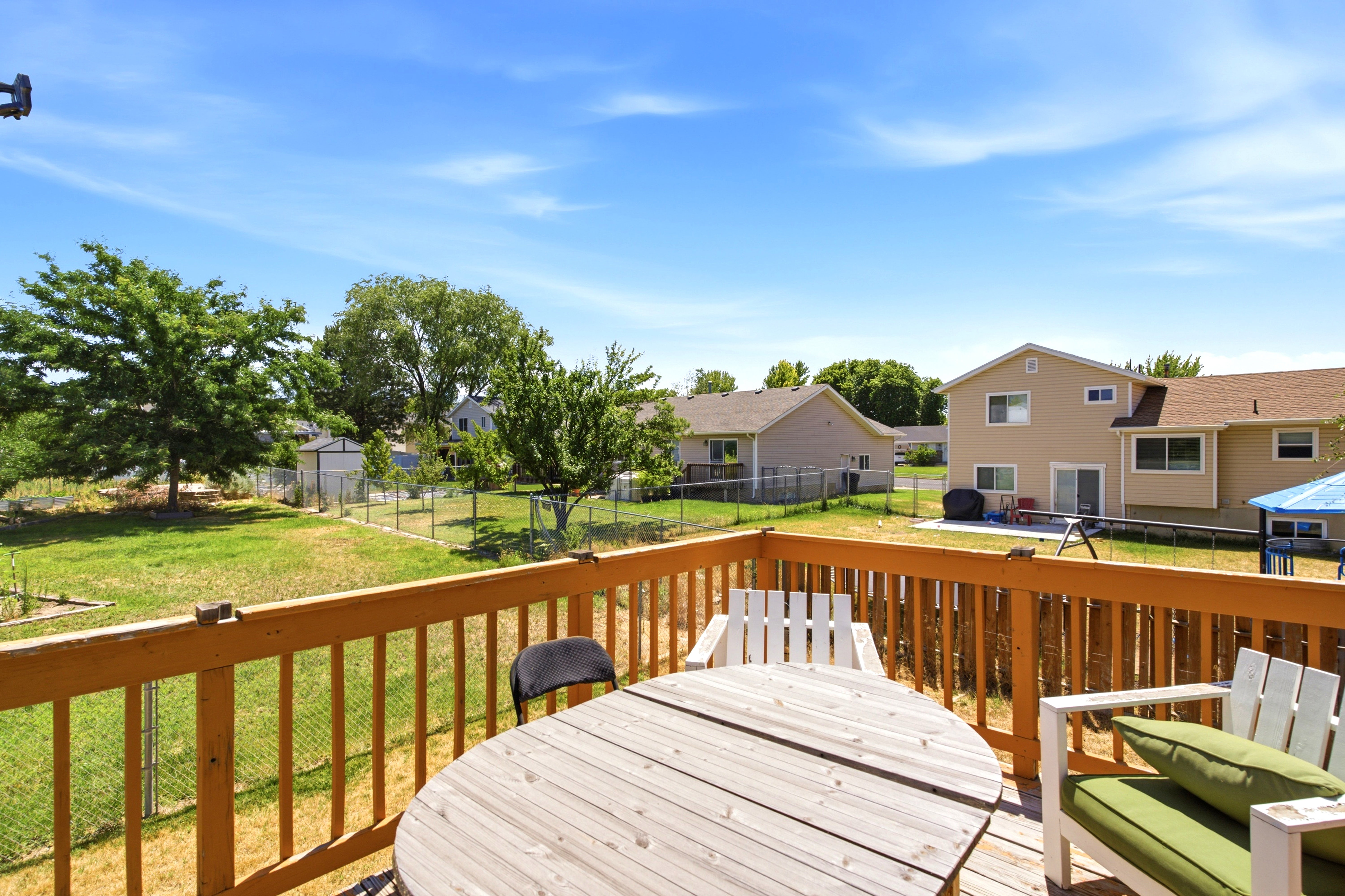 Wood deck with wood railing, offering views of a fenced backyard with mature trees