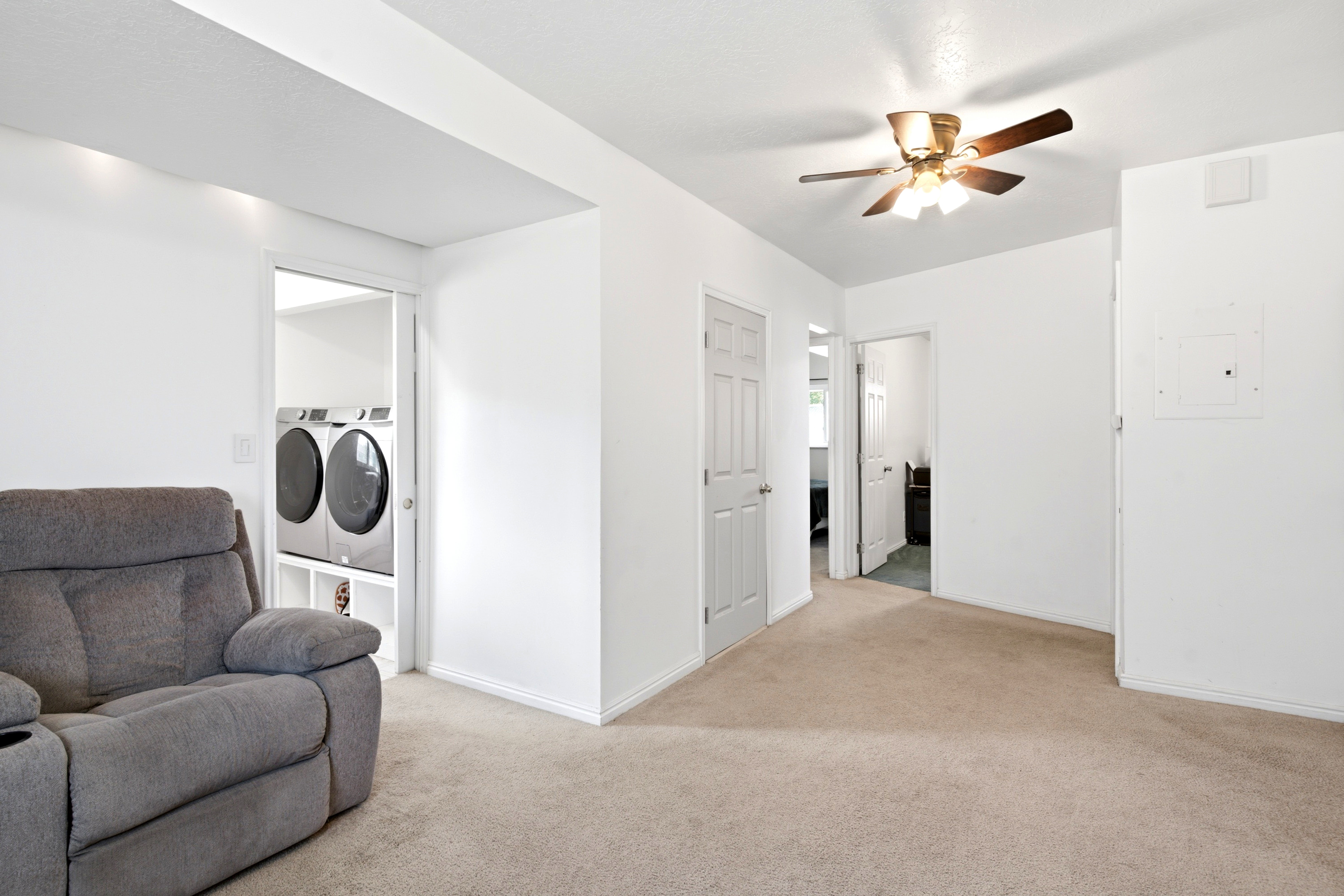 Carpeted interior space featuring a laundry area with stacked appliances, white walls, and a ceiling fan