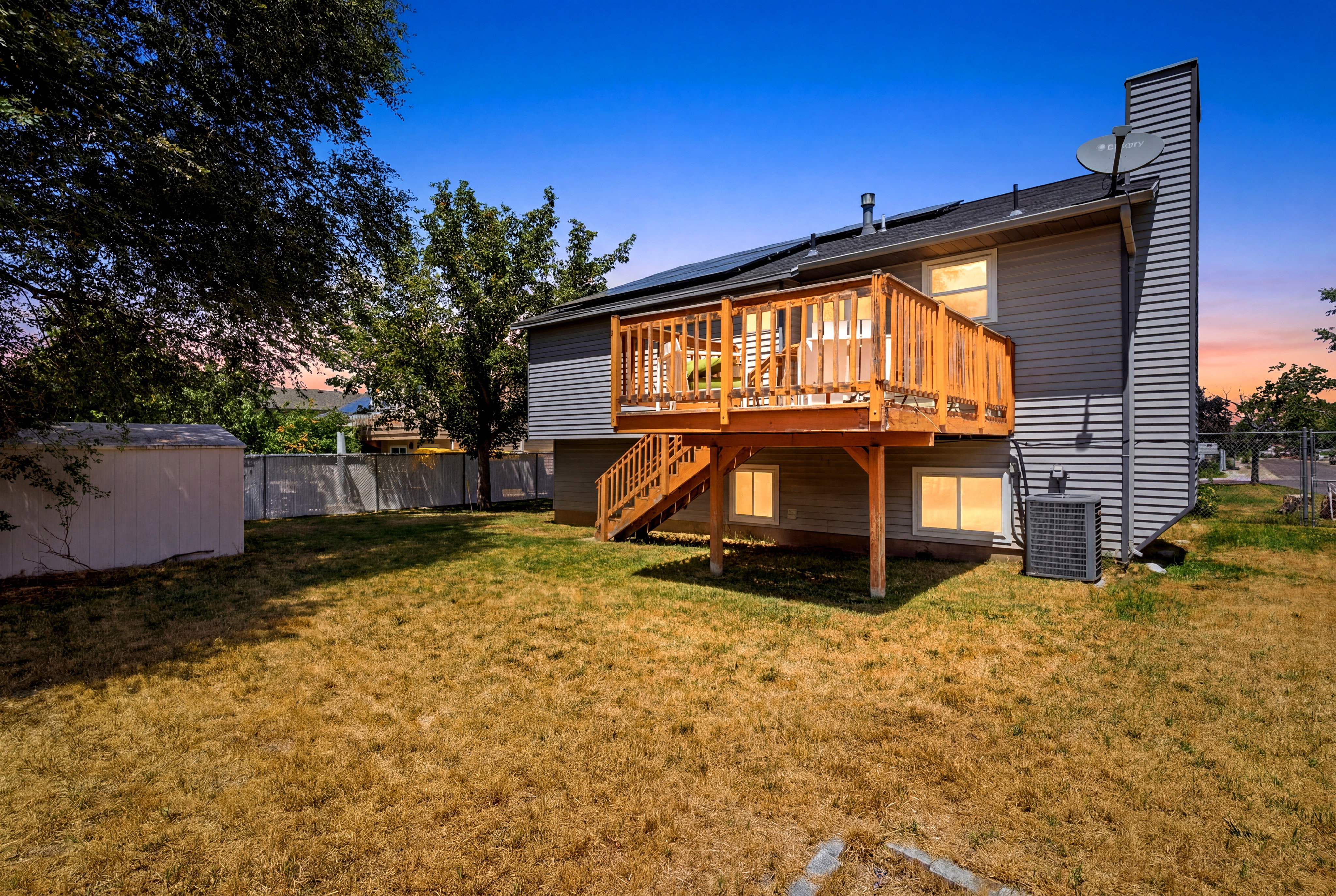 Expansive backyard featuring a raised wood deck with staircase, ground-level windows, and a detached storage shed