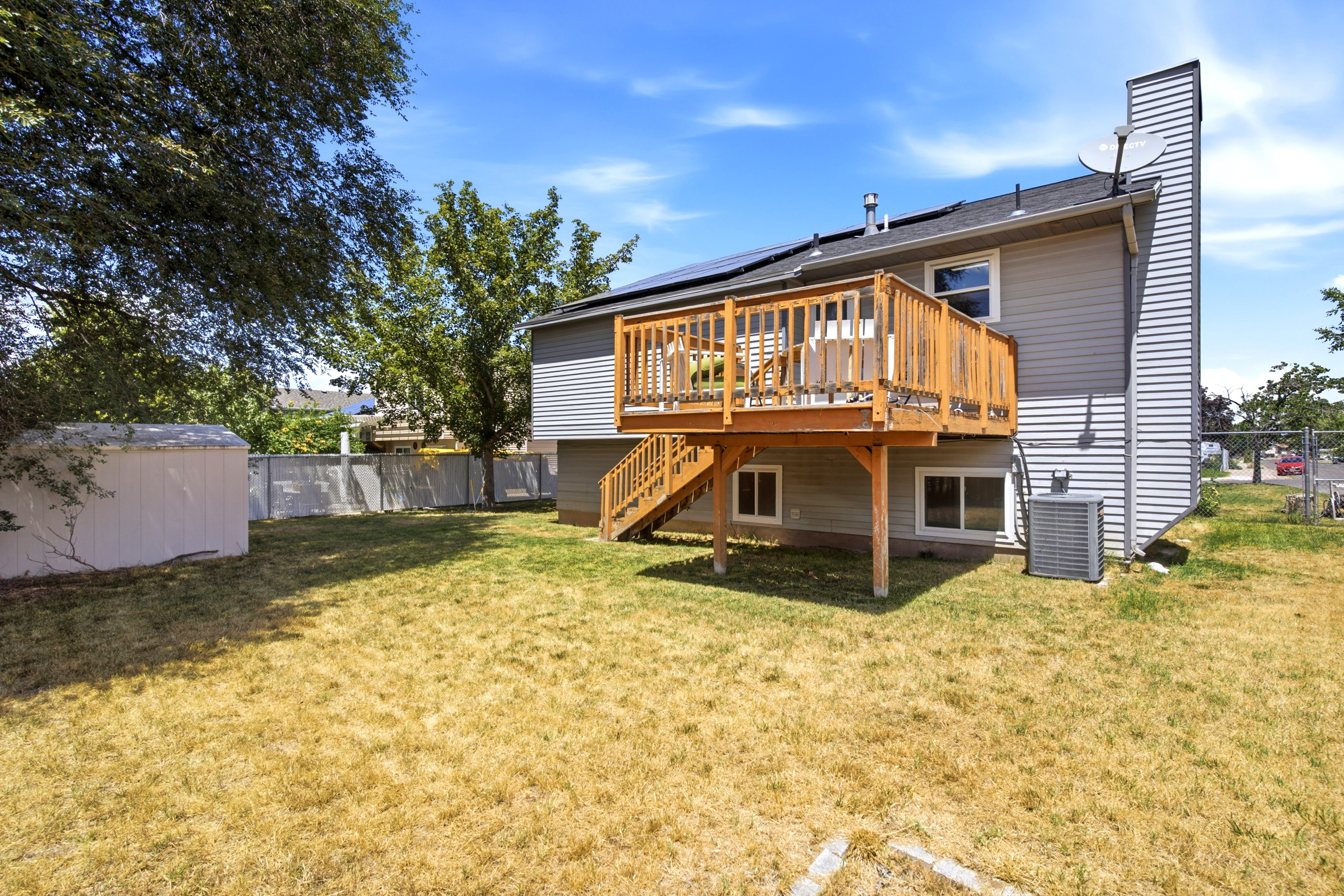 Expansive backyard featuring a tiered wooden deck with railing, gray horizontal siding, and a storage shed