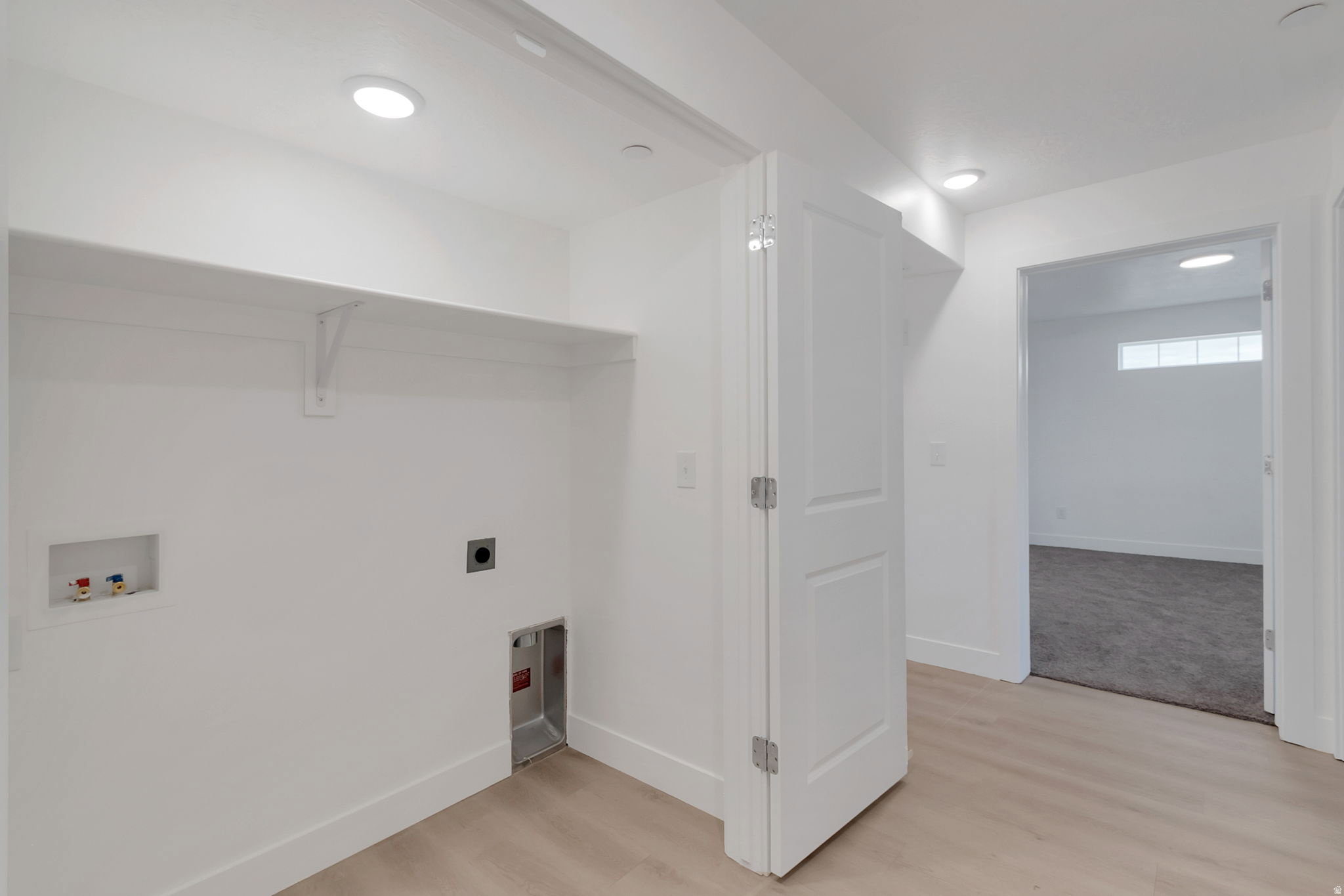Dedicated laundry area featuring a built-in shelf, appliance hookups, overhead lighting, and wood-finish flooring