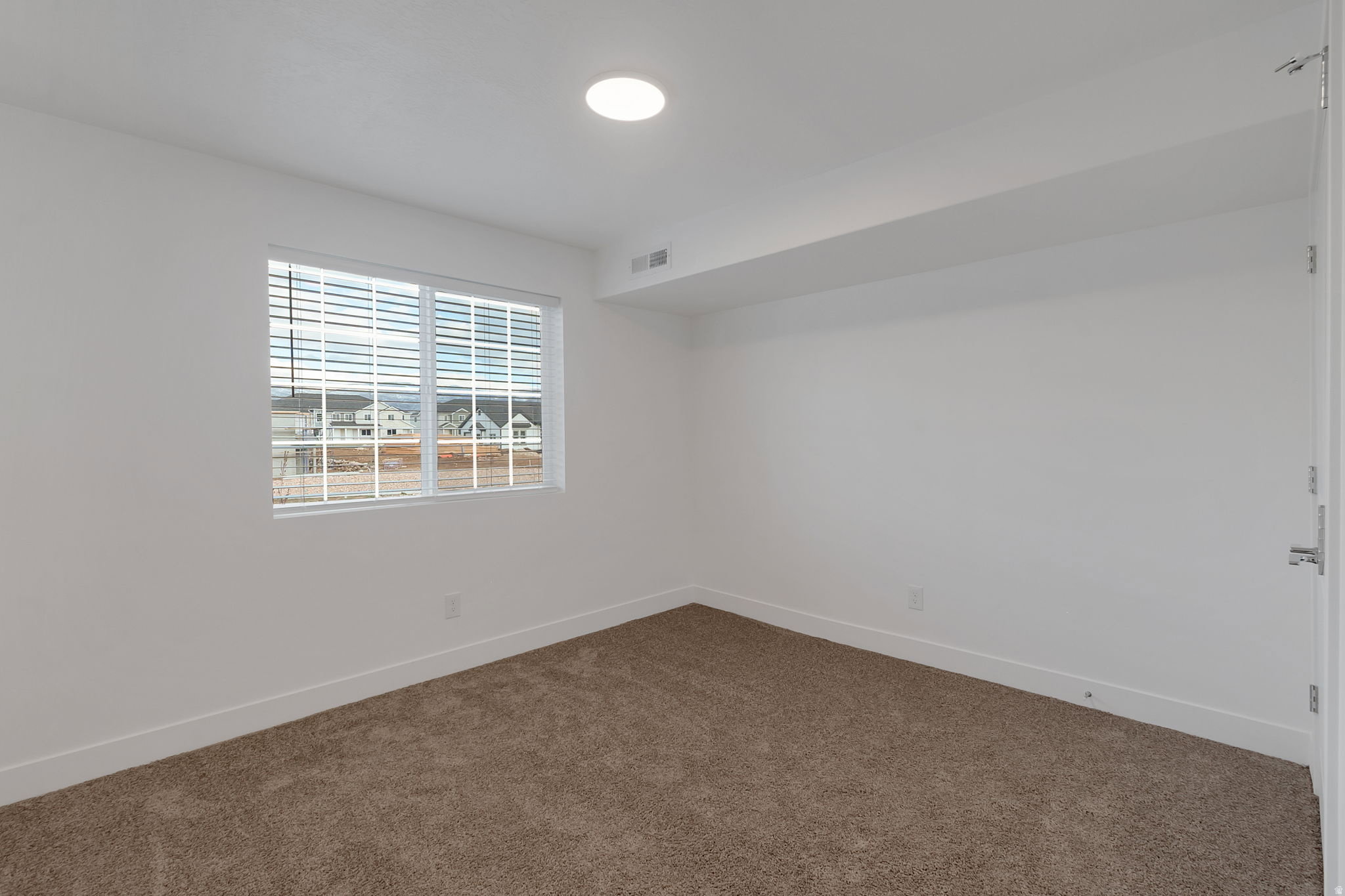 Neutral-toned carpet flooring and white walls define this space, featuring a single window with horizontal blinds