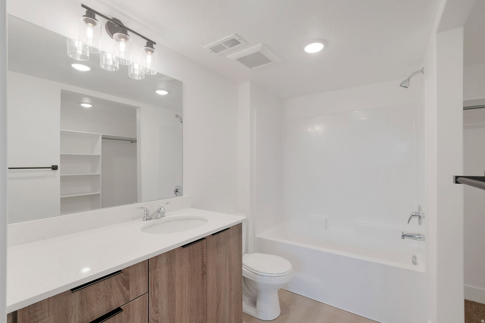 Bathroom featuring a wood-finish vanity with quartz countertop, undermount sink, and a framed mirror