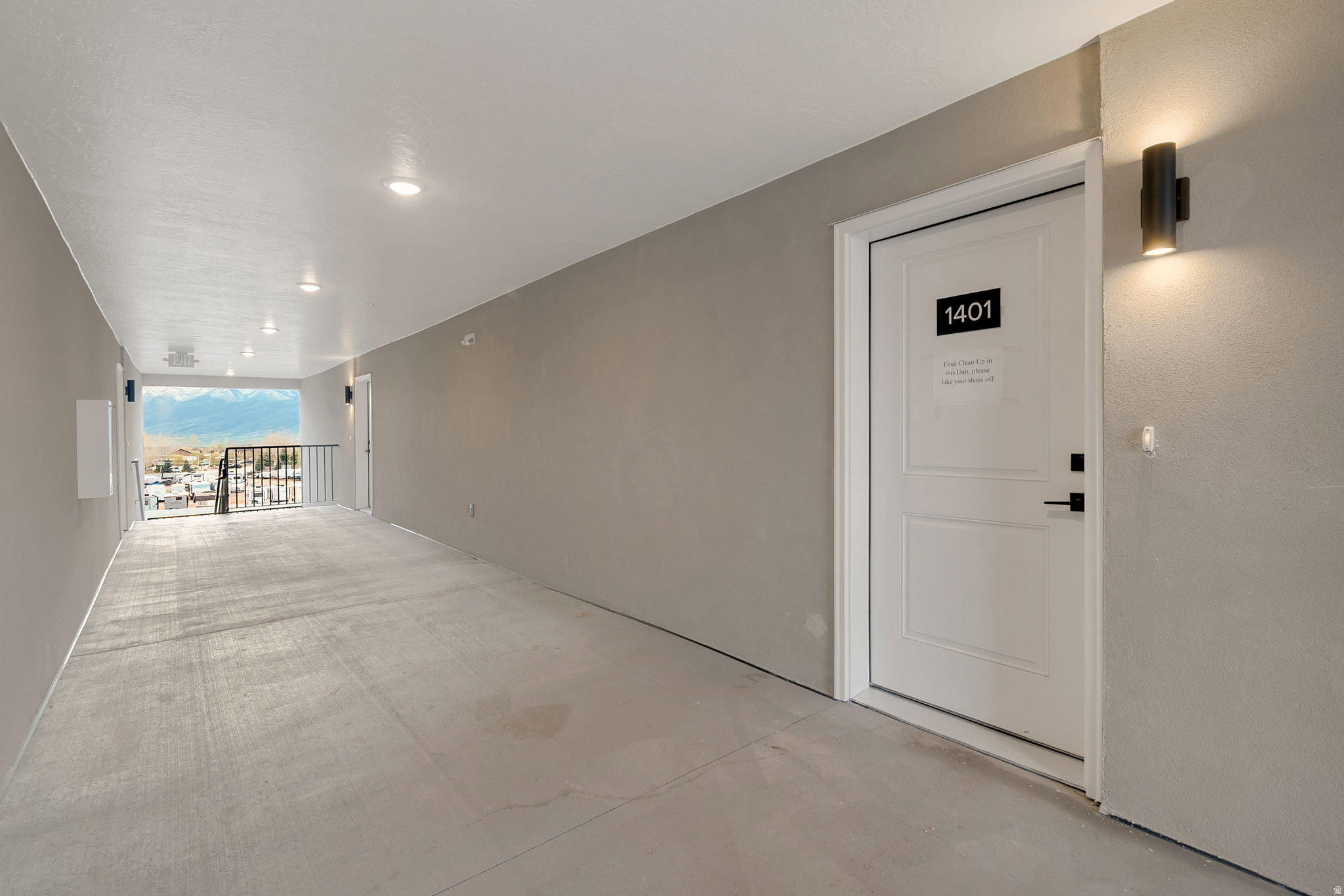 Exterior corridor with a mountain backdrop, featuring a white paneled door with black hardware, wall-mounted sconce lighting, and recessed ceiling lights