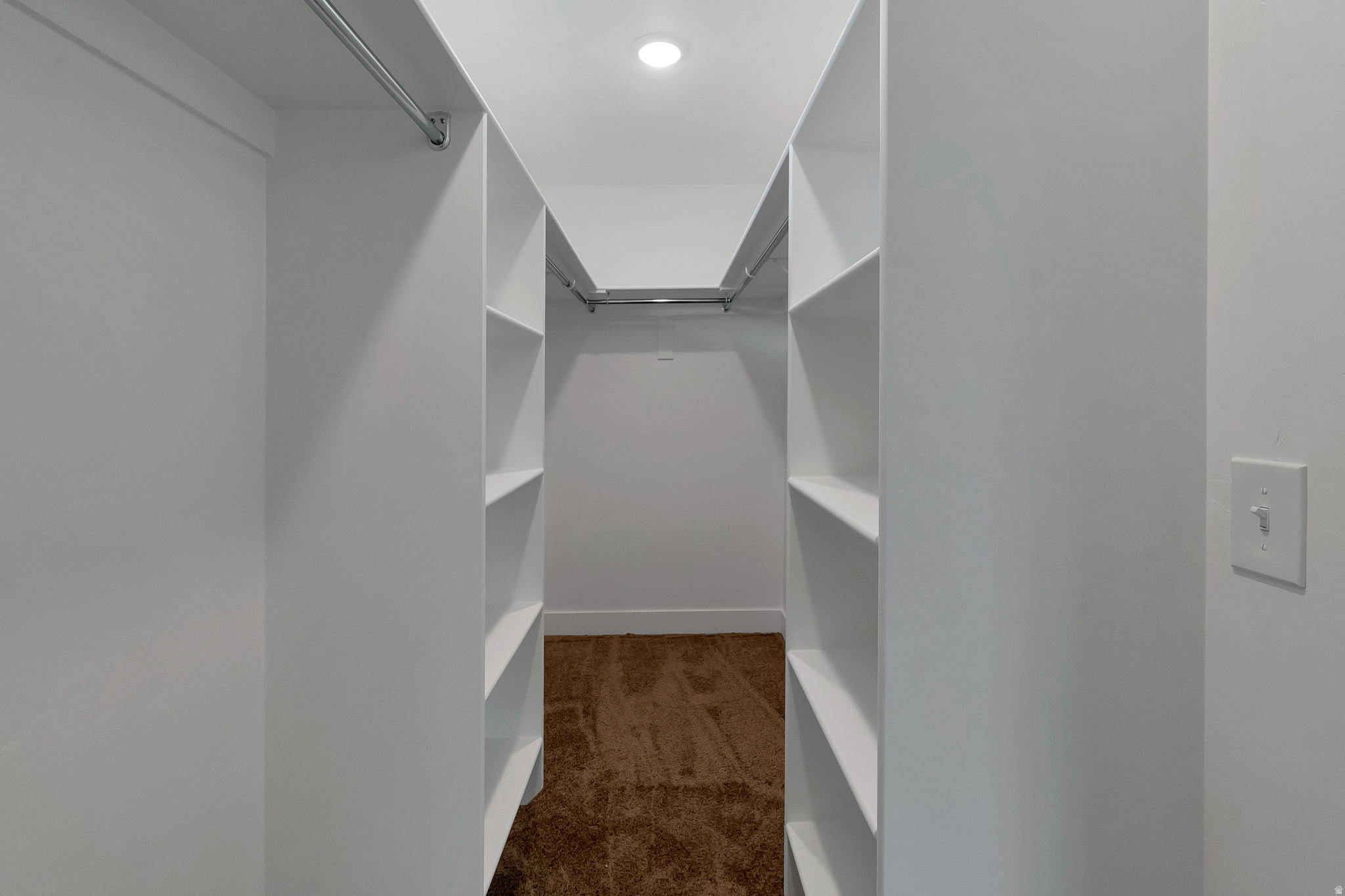Walk-in closet featuring extensive built-in shelving, multiple hanging rods, recessed lighting, and brown carpet flooring