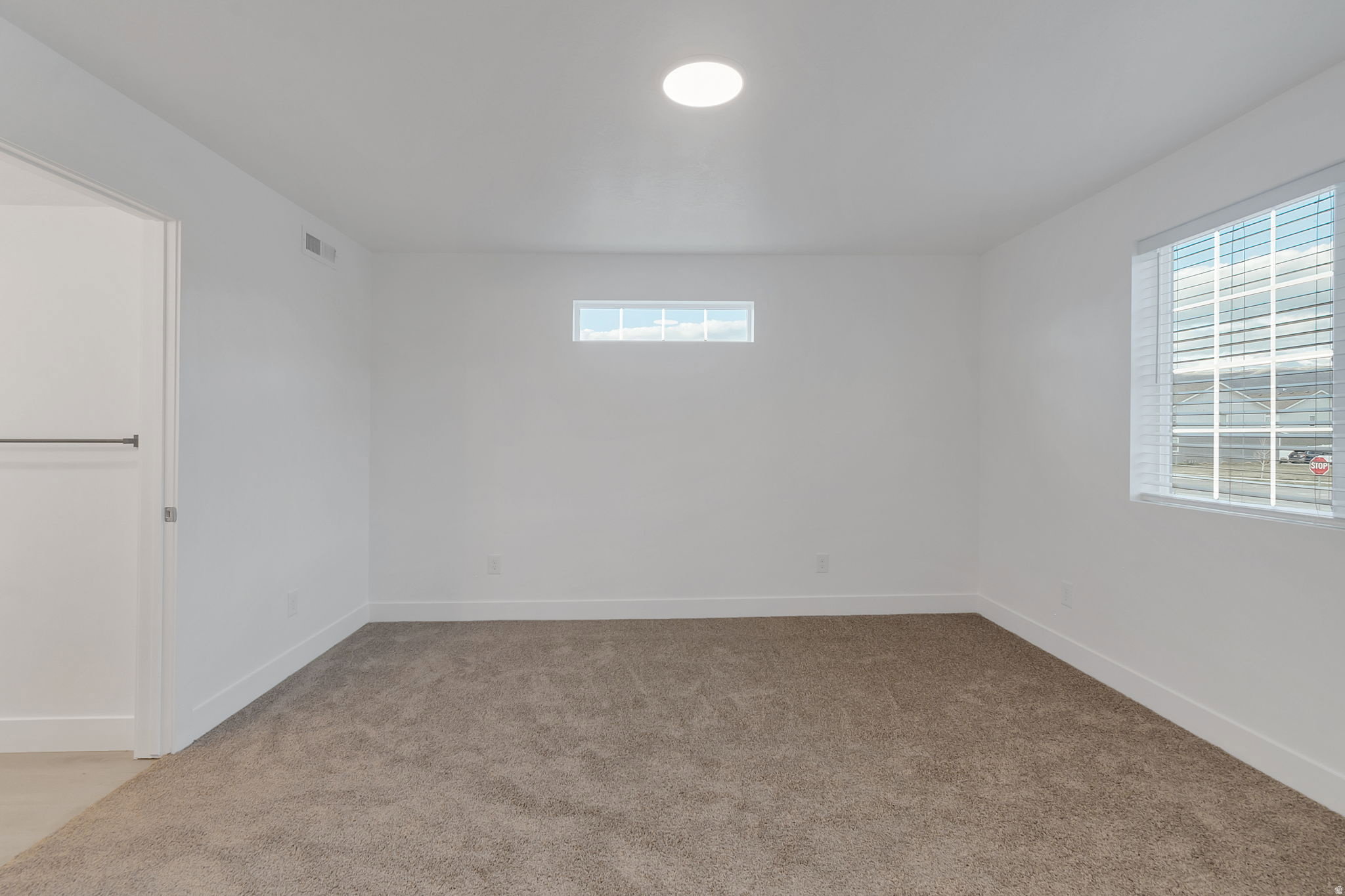Carpeted room with white walls, featuring a large window with blinds, an upper transom window, and a recessed ceiling light