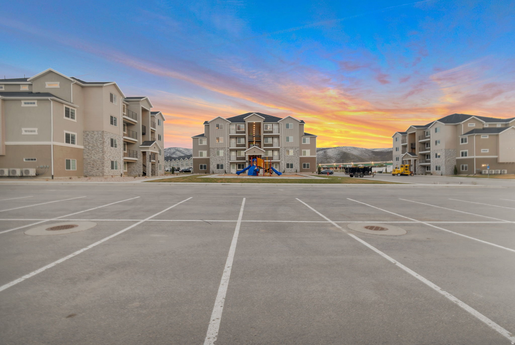Multi-story buildings featuring balconies, a central playground area, and ample exterior parking