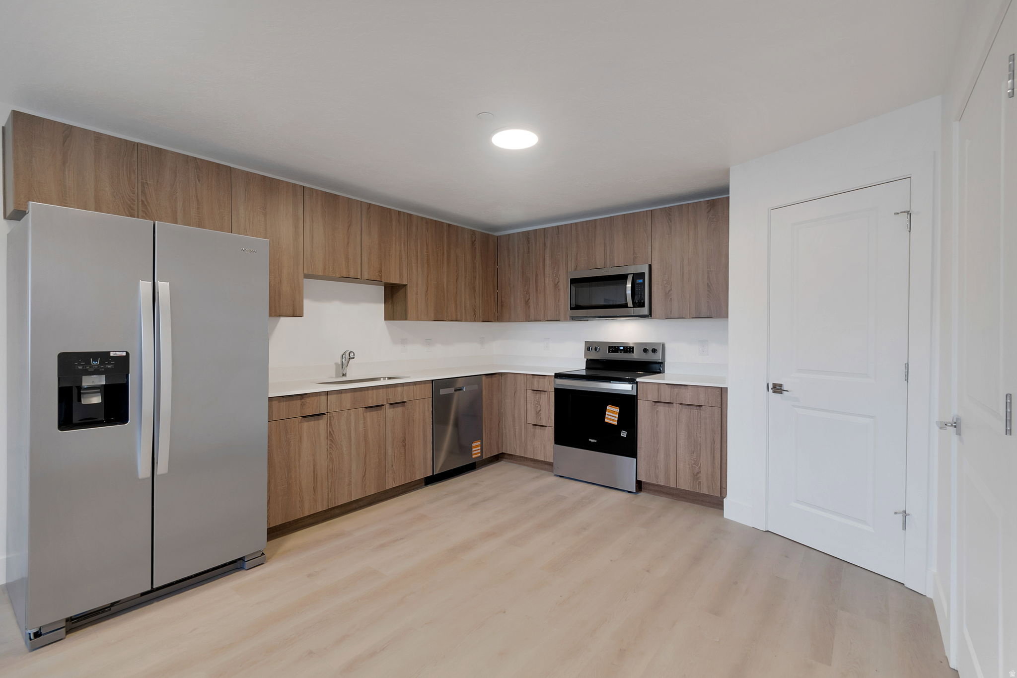 Modern kitchen featuring wood-finish cabinetry, white countertops, and stainless steel appliances including a side-by-side refrigerator, range, microwave, and dishwasher