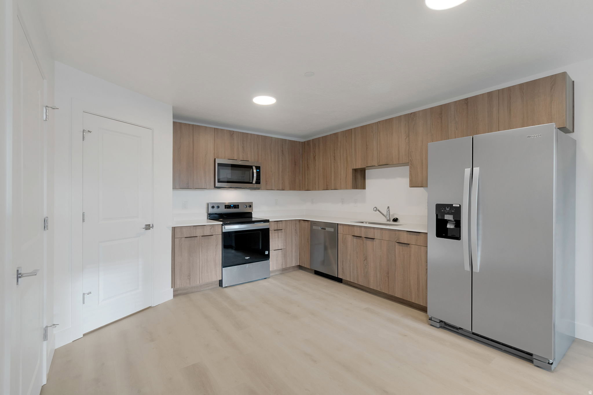 L-shaped kitchen featuring wood-finish cabinetry, stainless steel appliances, and light-toned countertops