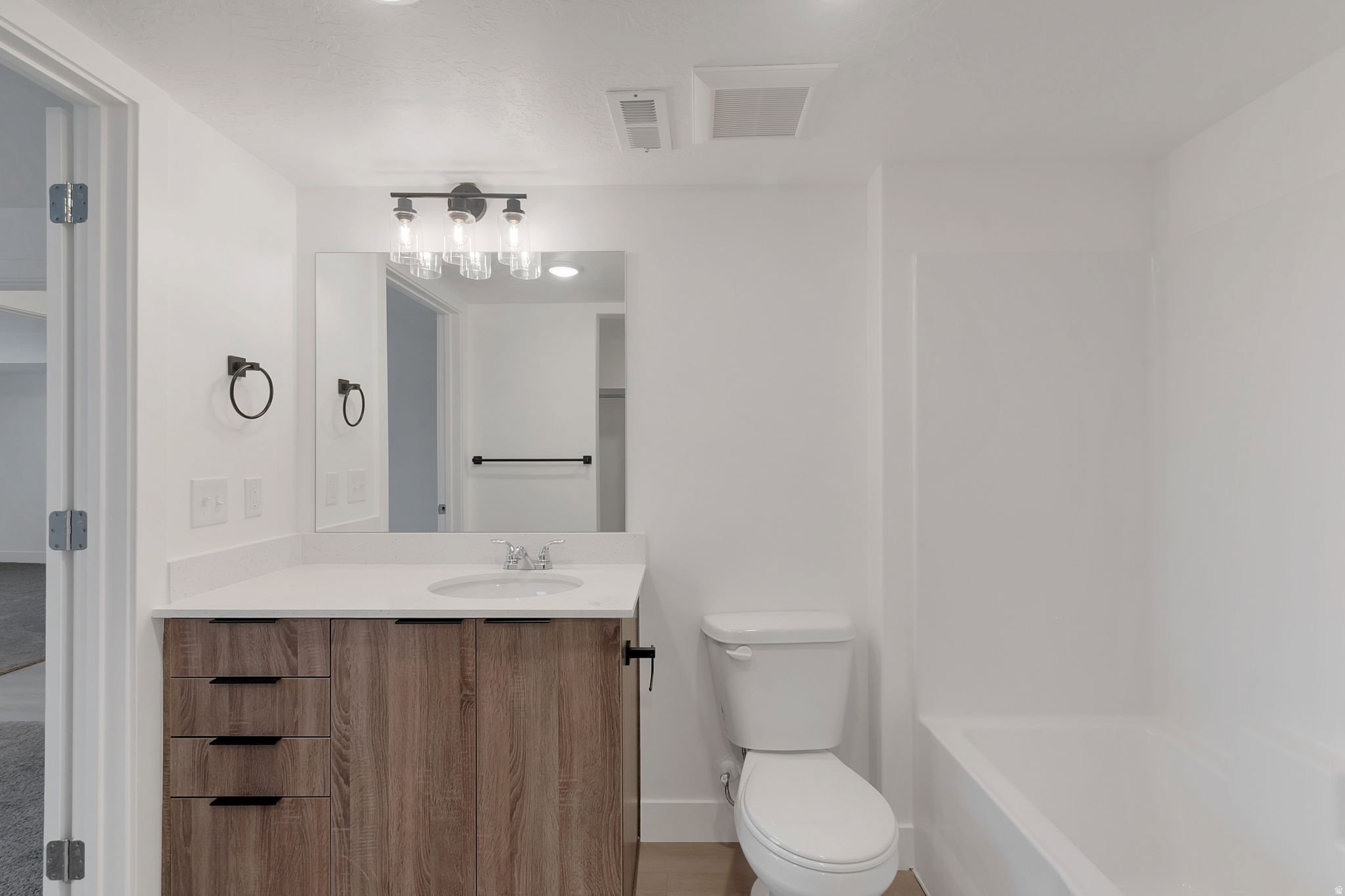 Bathroom featuring a wood-finish vanity with an integrated sink, white countertop, and contemporary lighting fixture