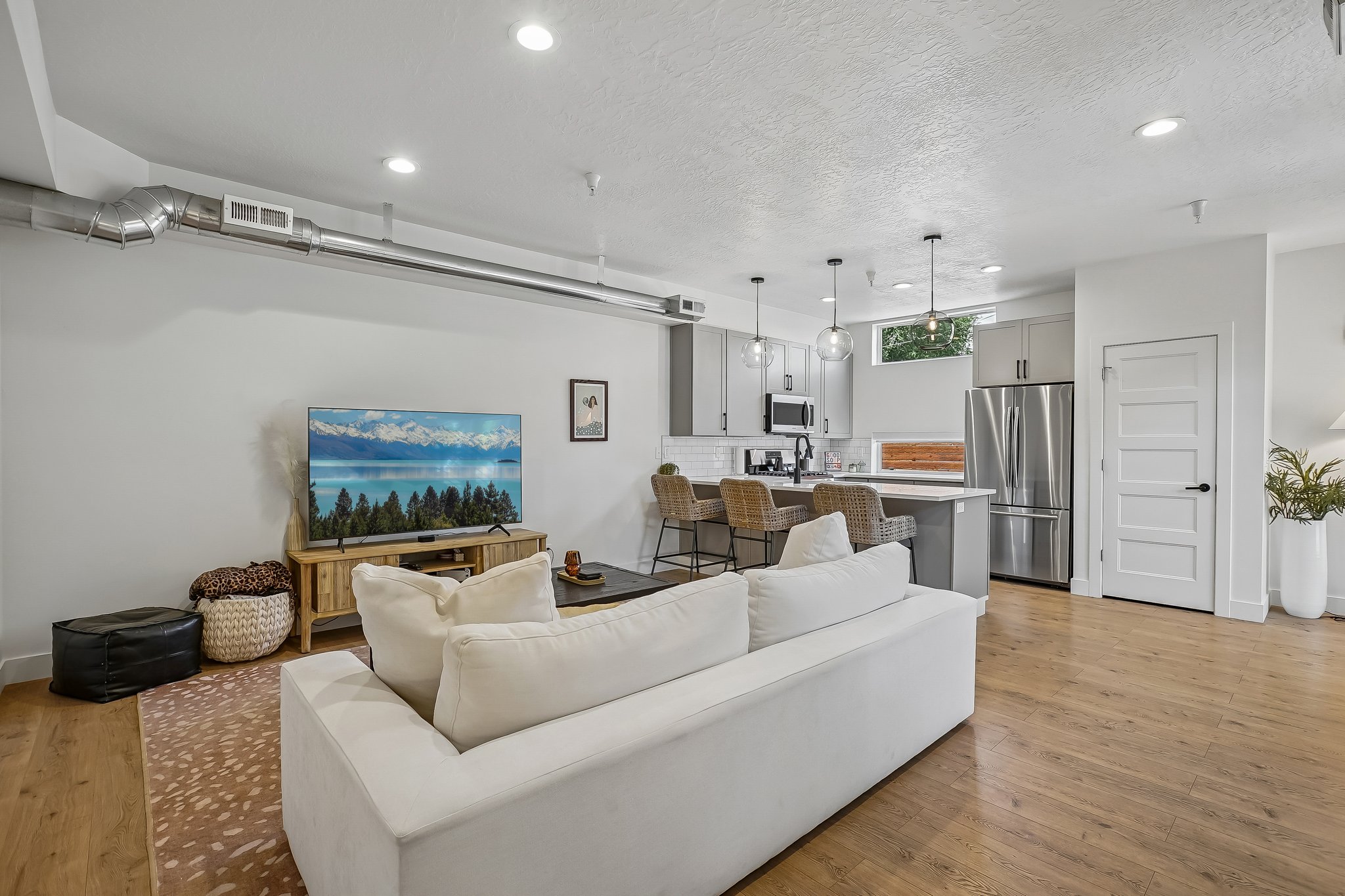 Open-concept living area featuring wood-finish flooring, recessed lighting, and exposed ductwork