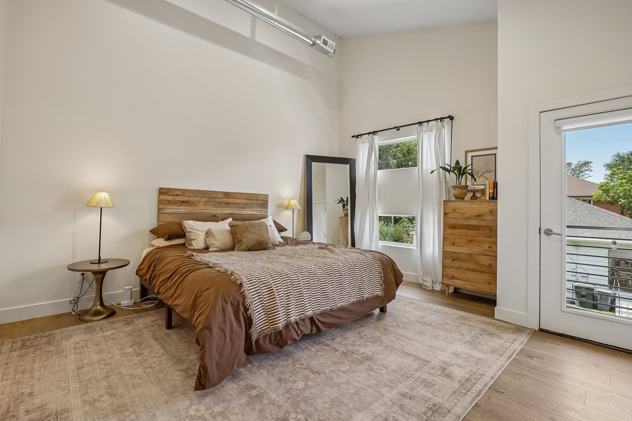 Spacious room featuring light wood-finish flooring, high ceilings, a balcony access door, and multiple windows with white blinds