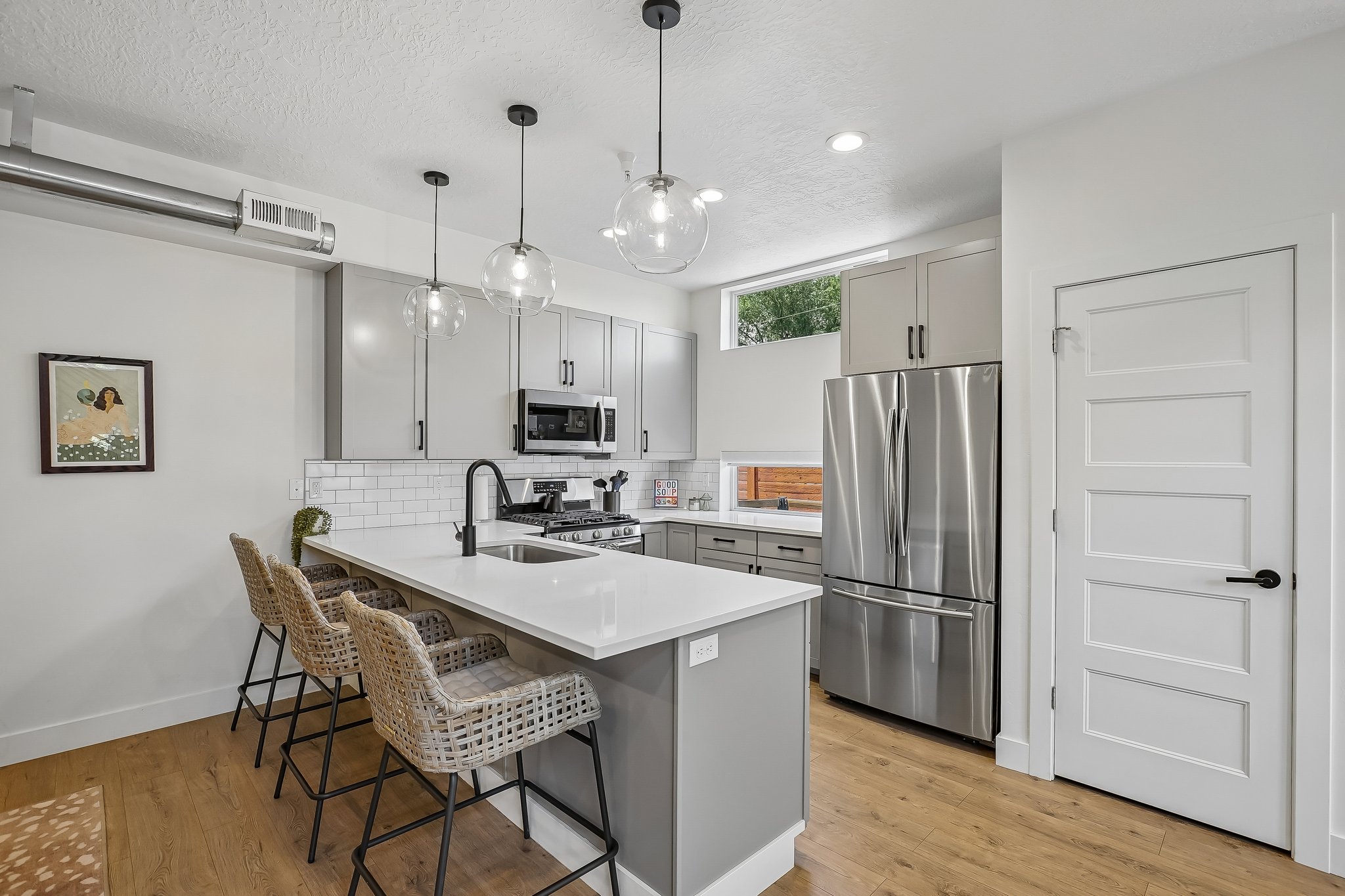 Contemporary kitchen featuring a white countertop island with seating, pendant lighting, stainless steel appliances, light gray cabinetry, and wood-finish flooring