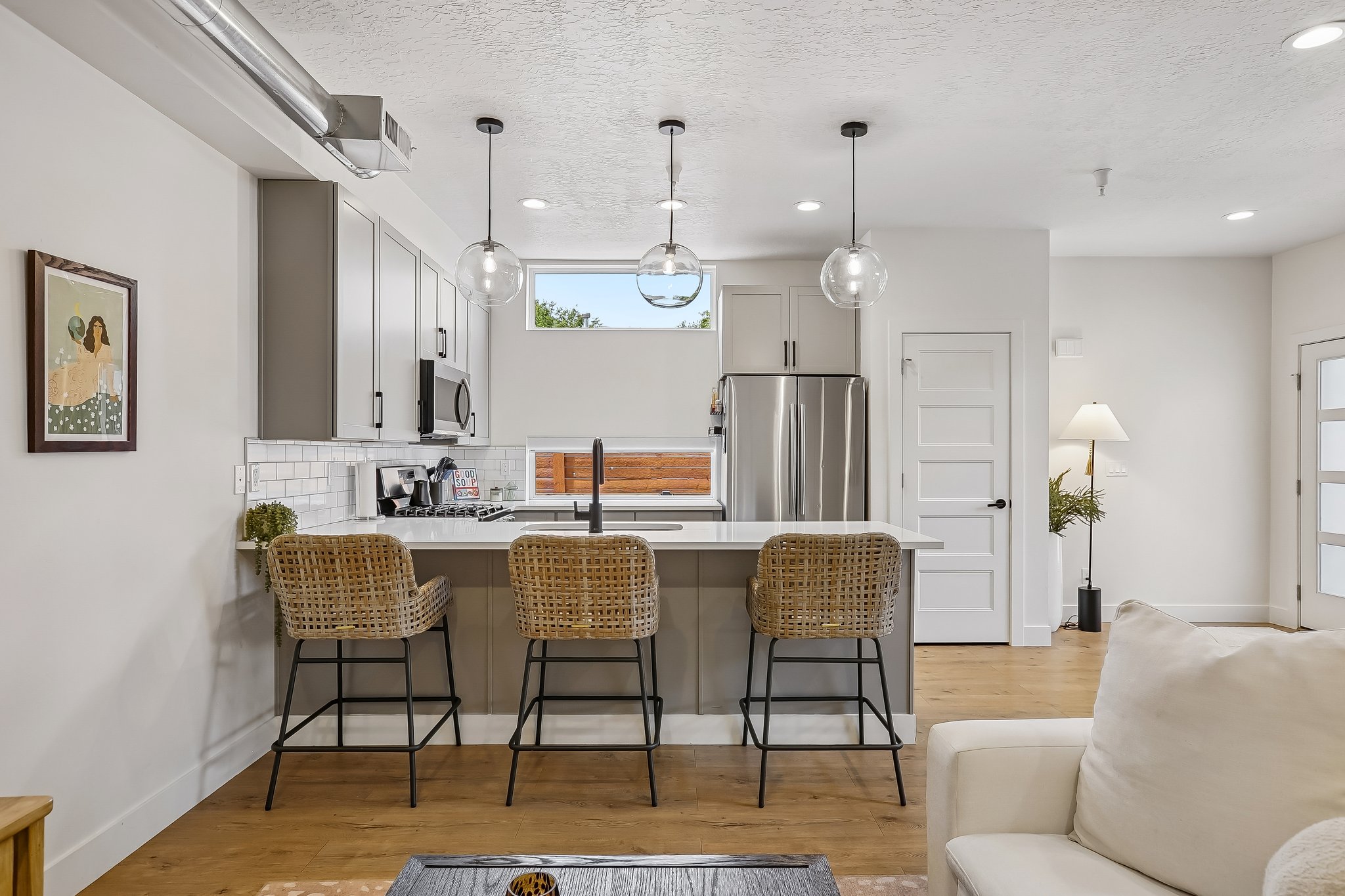 Modern kitchen featuring a breakfast bar with pendant lighting, stainless steel appliances, light gray cabinetry, and a white subway tile backsplash