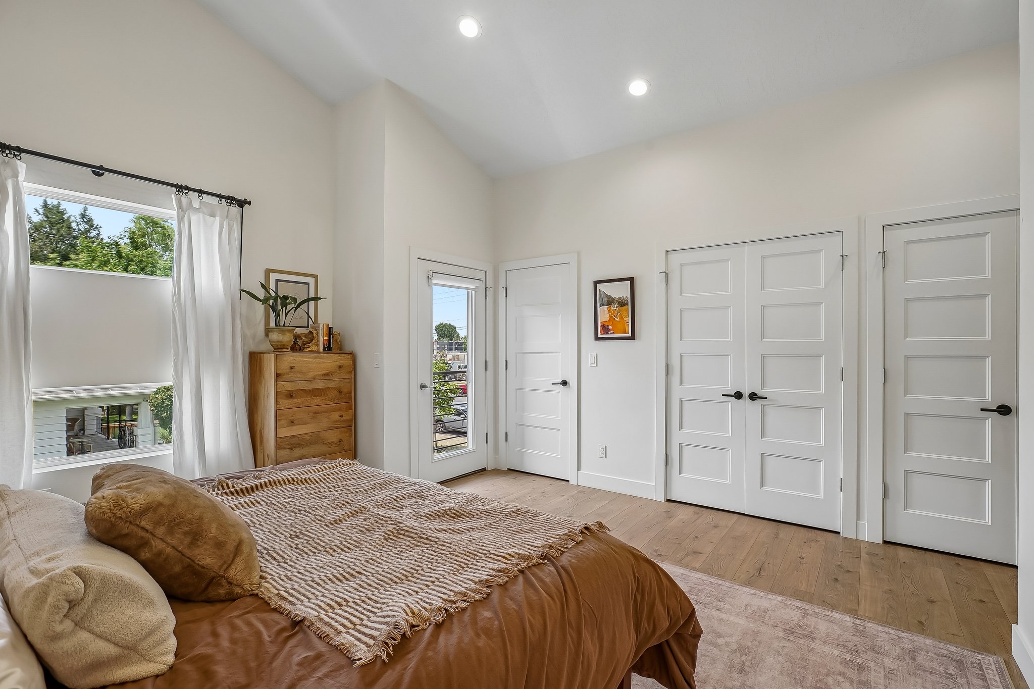 Spacious room featuring vaulted ceilings, recessed lighting, wood-finish flooring, and multiple five-panel doors with matte black hardware