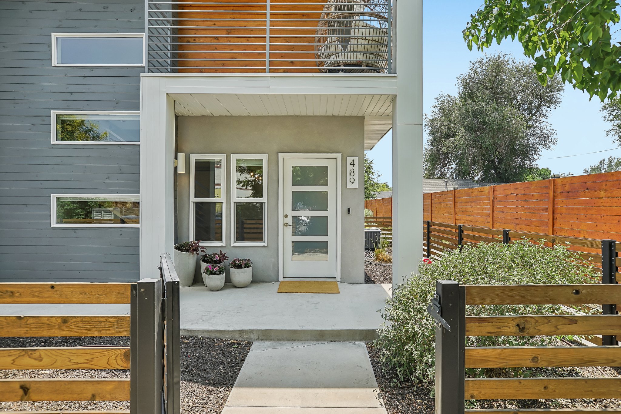 Contemporary exterior featuring horizontal wood siding, a second-story balcony with slatted wood details, a privacy fence crafted from horizontal wood planks, and a concrete entry path leading to the front door