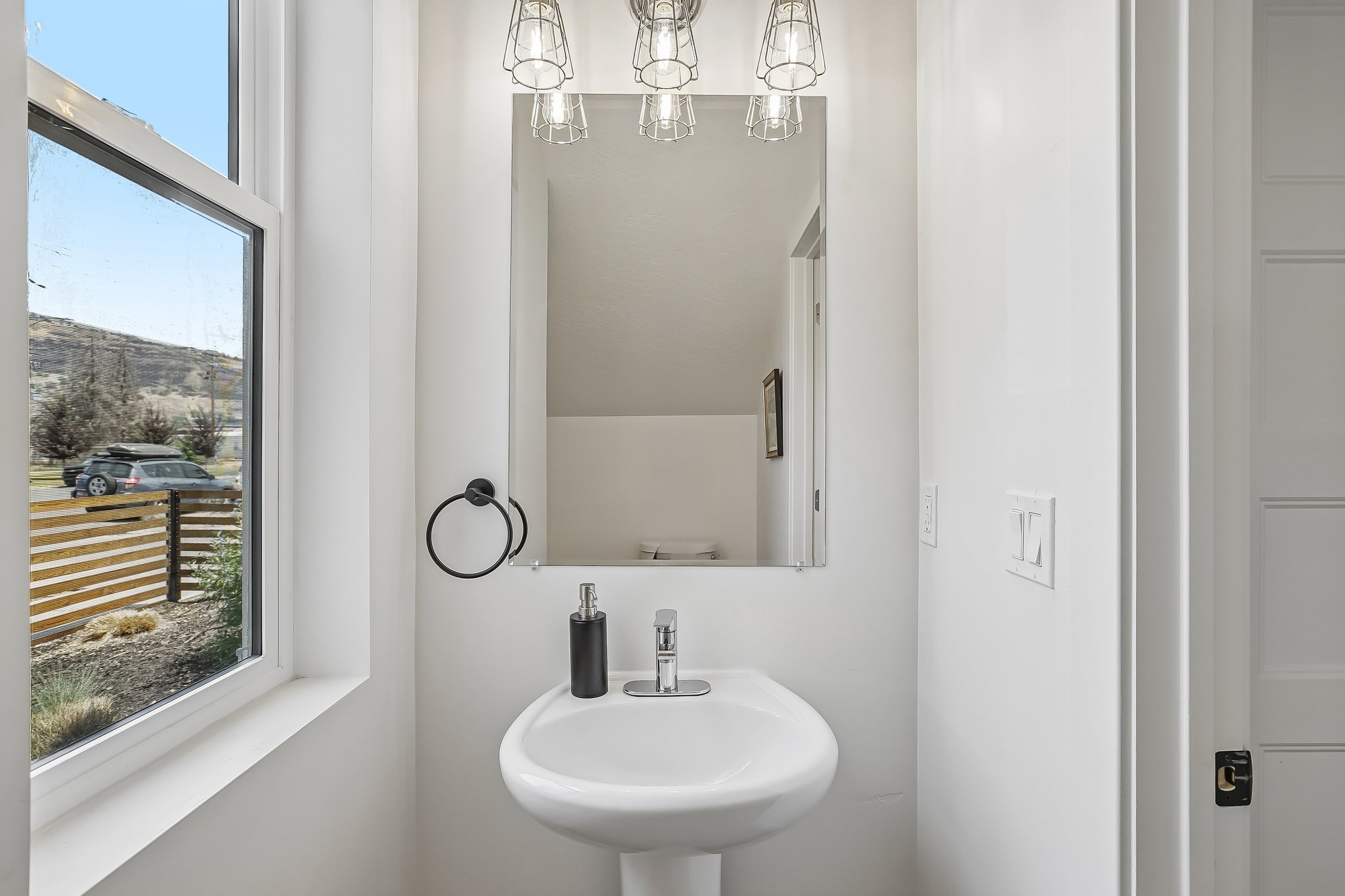 Pedestal sink featuring a chrome faucet, black towel ring, and overhead industrial-style vanity lighting