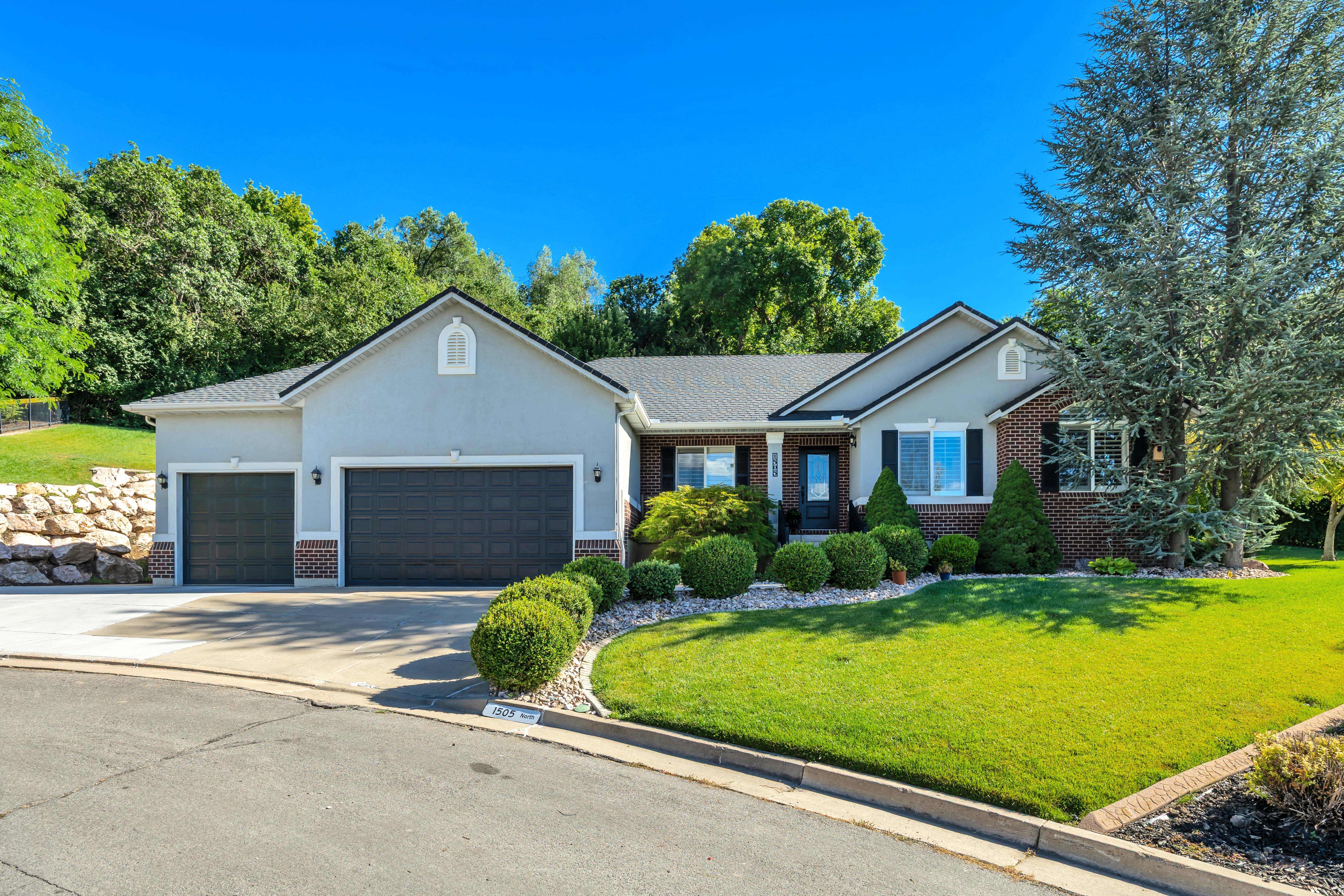 Ranch-style residence featuring a three-car garage, brick and stucco exterior, and a manicured lawn