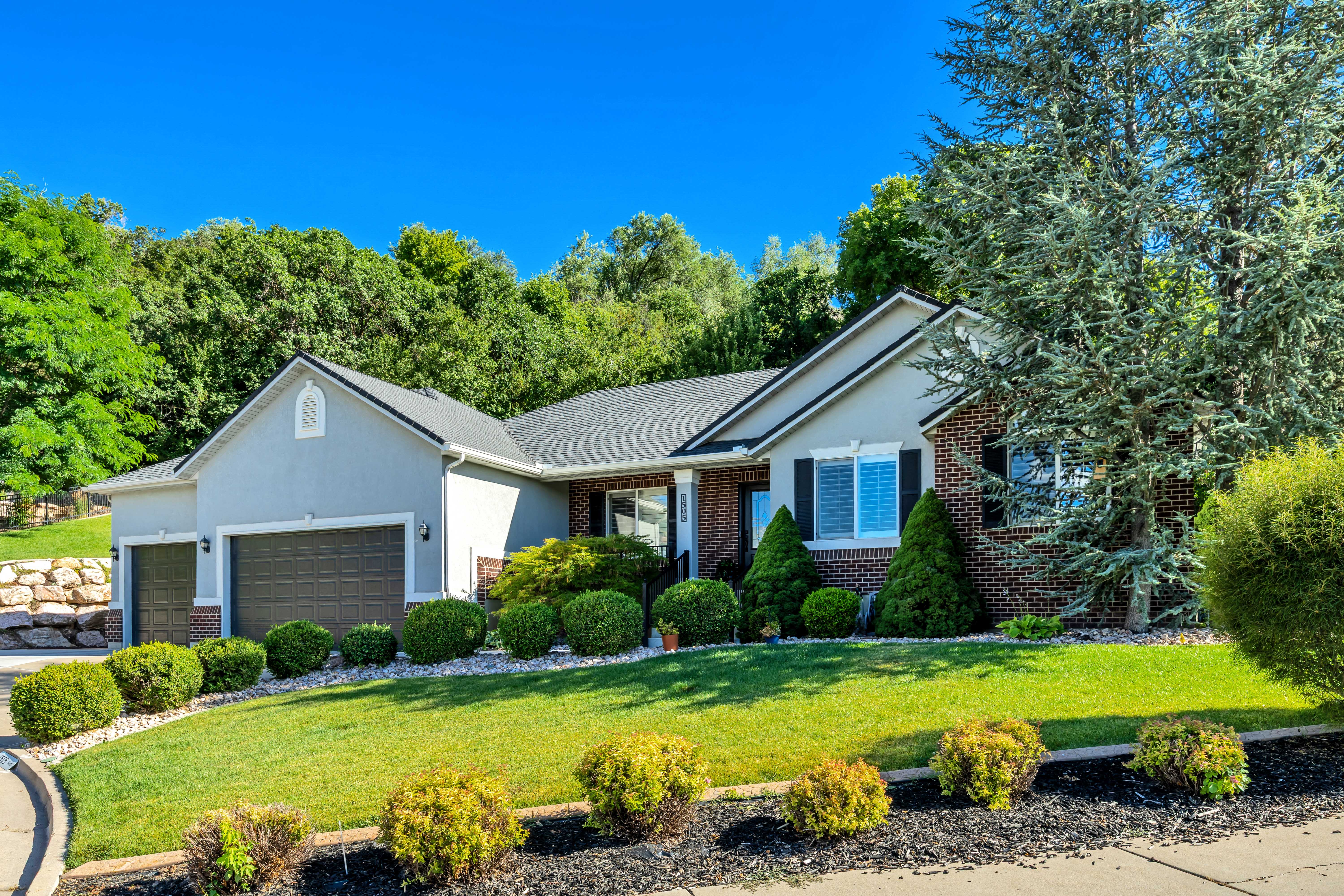 Ranch-style residence featuring stucco and brick, a dark shingle roof, and a three-car garage with panel doors