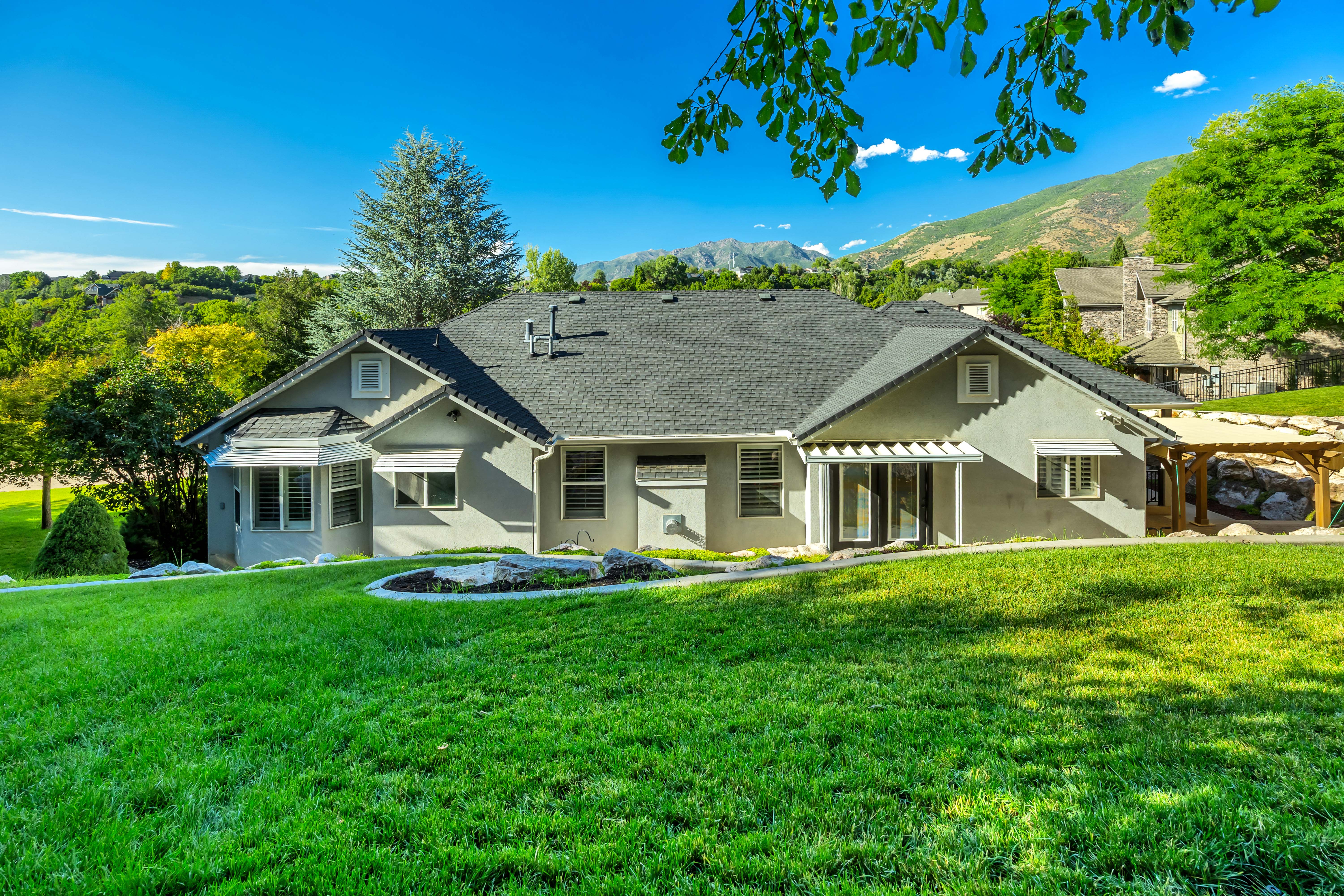 Expansive backyard featuring a manicured lawn, established landscaping, and a mountain backdrop
