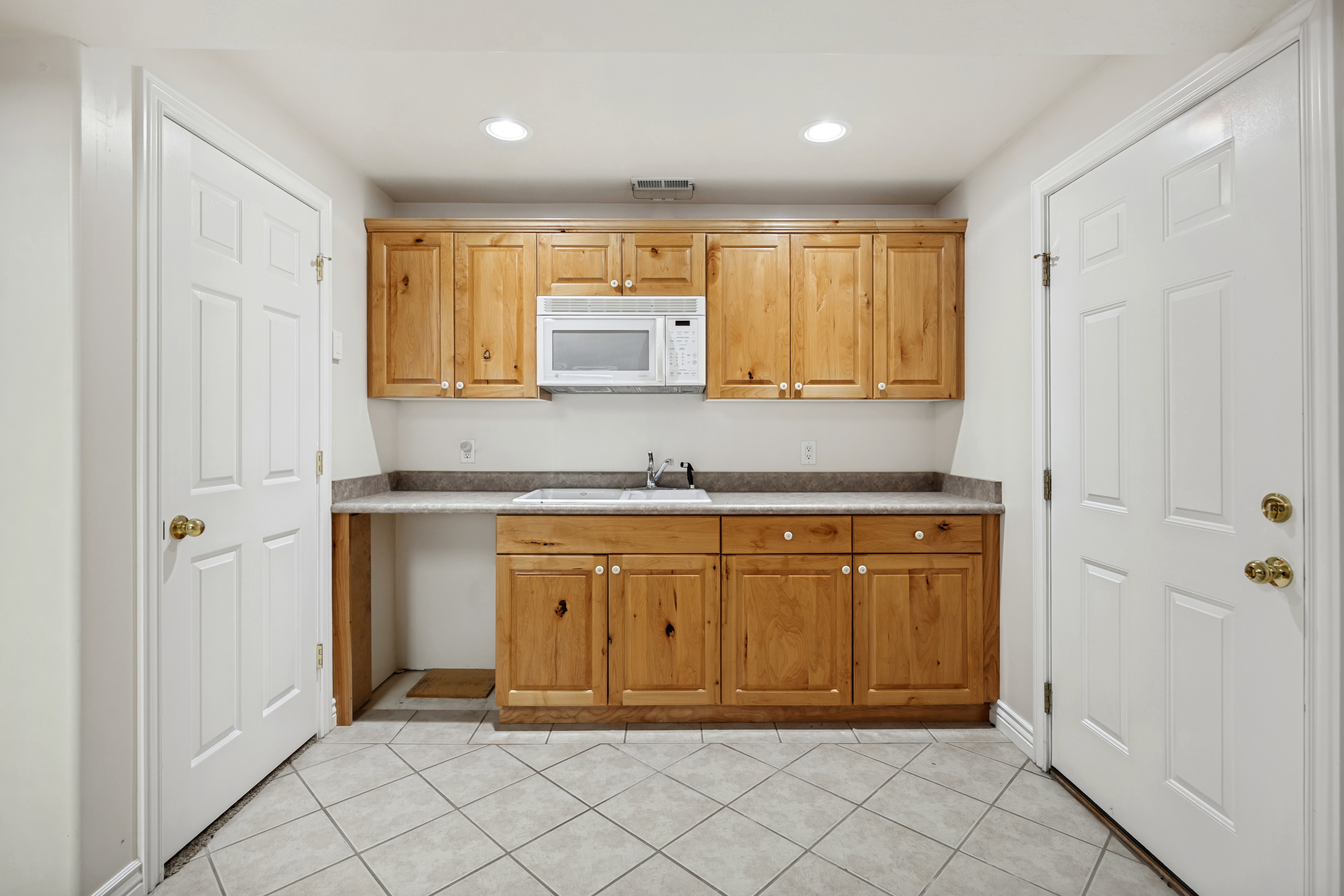 Kitchenette featuring wood cabinetry, laminate countertops, a stainless steel microwave, and a stainless steel sink with a single-handle faucet