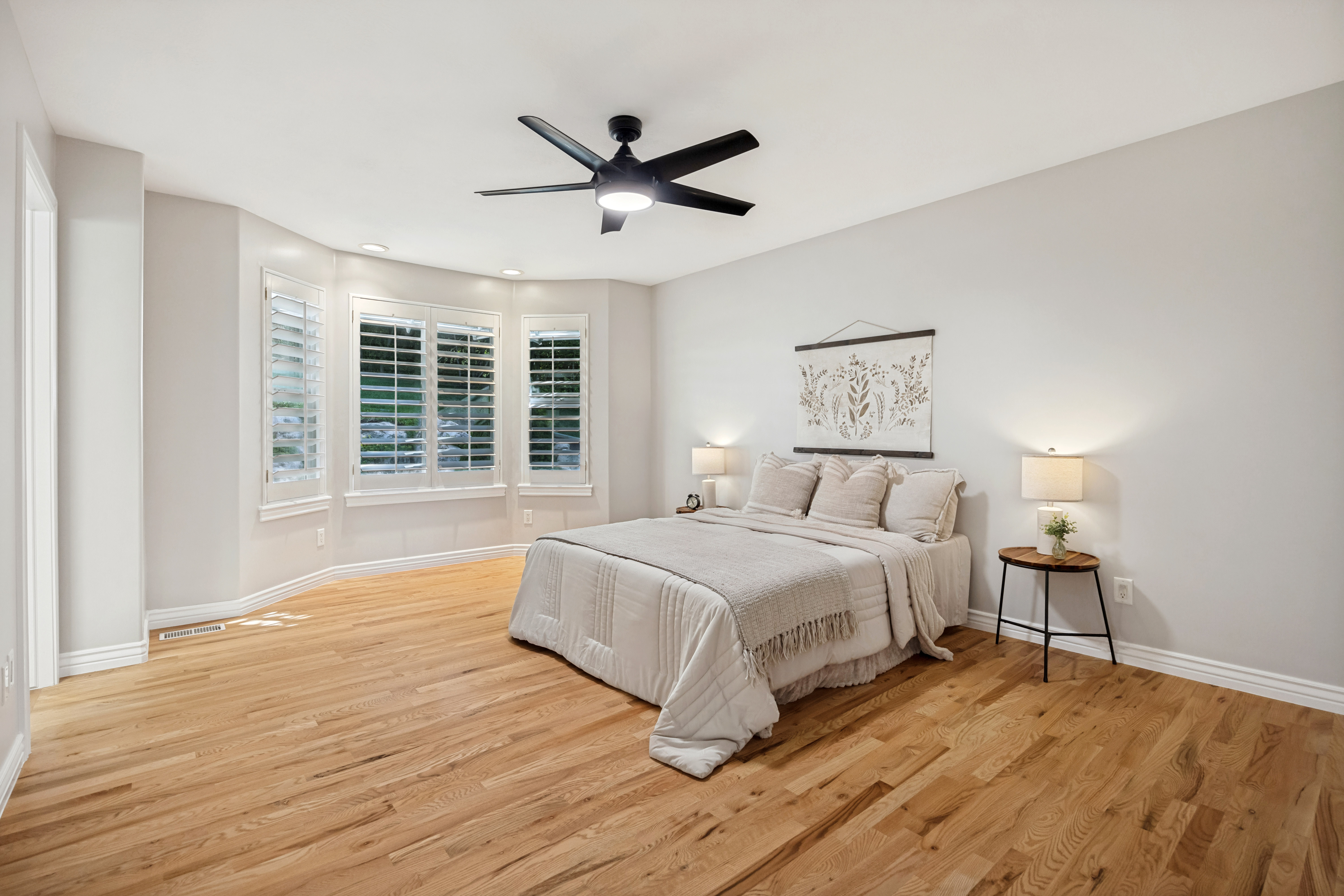 Bright and large primary bedroom featuring warm wood flooring, a contemporary ceiling fan, recessed lighting, and bay windows.