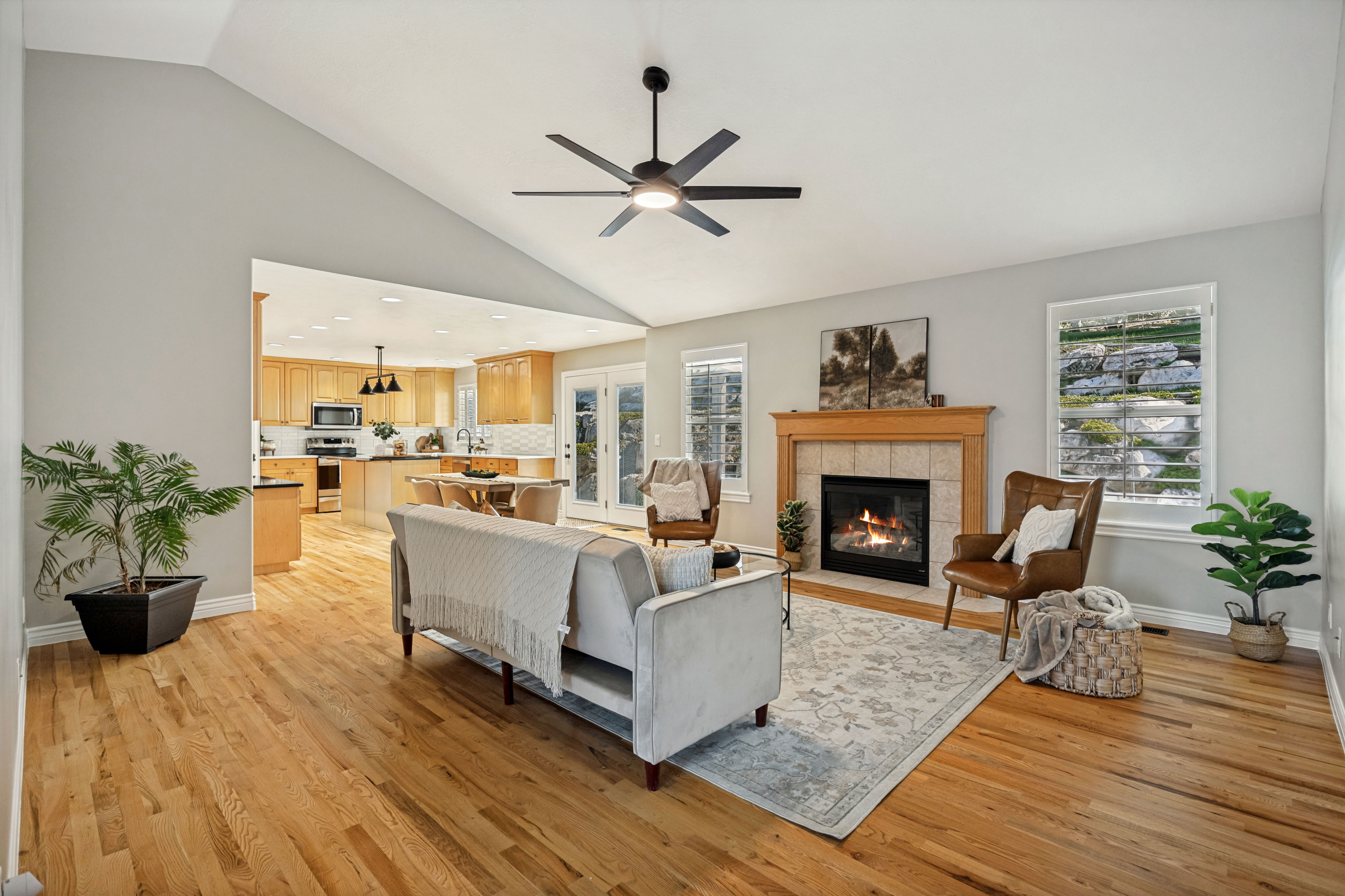 Vaulted living room featuring hardwood flooring, a ceiling fan, and a fireplace with a wood mantel