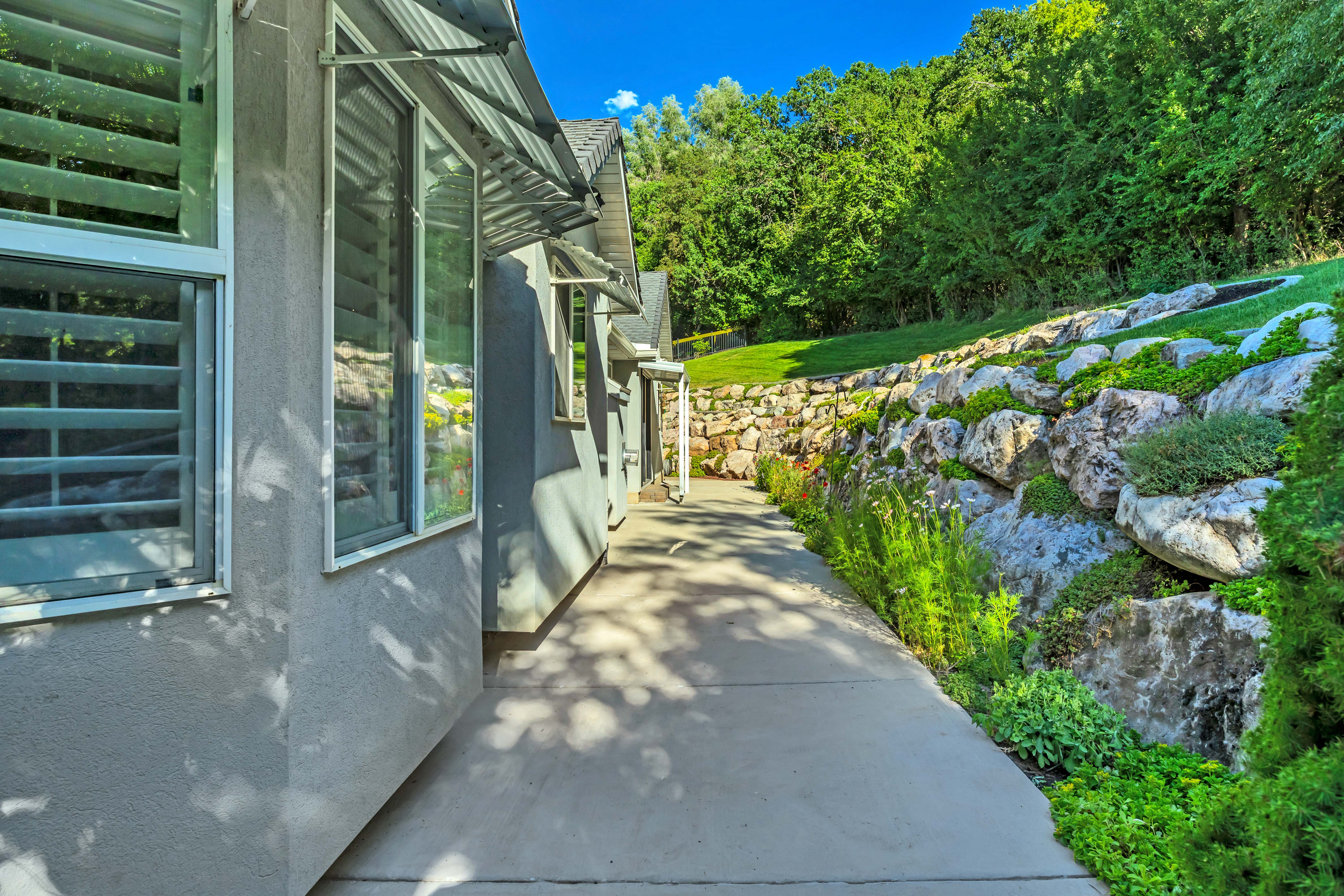Concrete pathway bordering a stucco exterior with multiple windows featuring louvered shutters and protective awnings