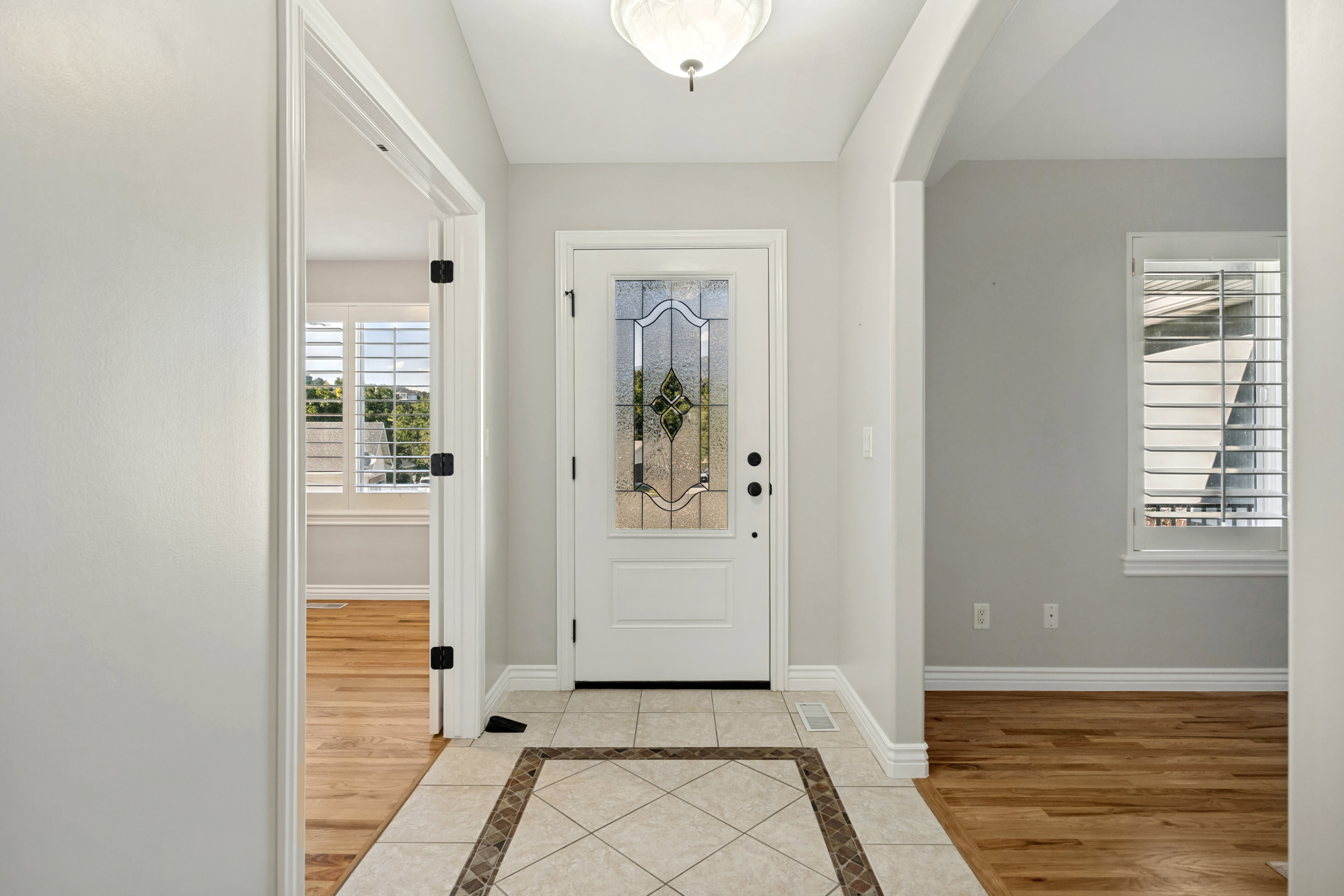 Entryway featuring a decorative glass front door, tile flooring with a patterned inlay, an arched doorway, and plantation shutters on visible windows