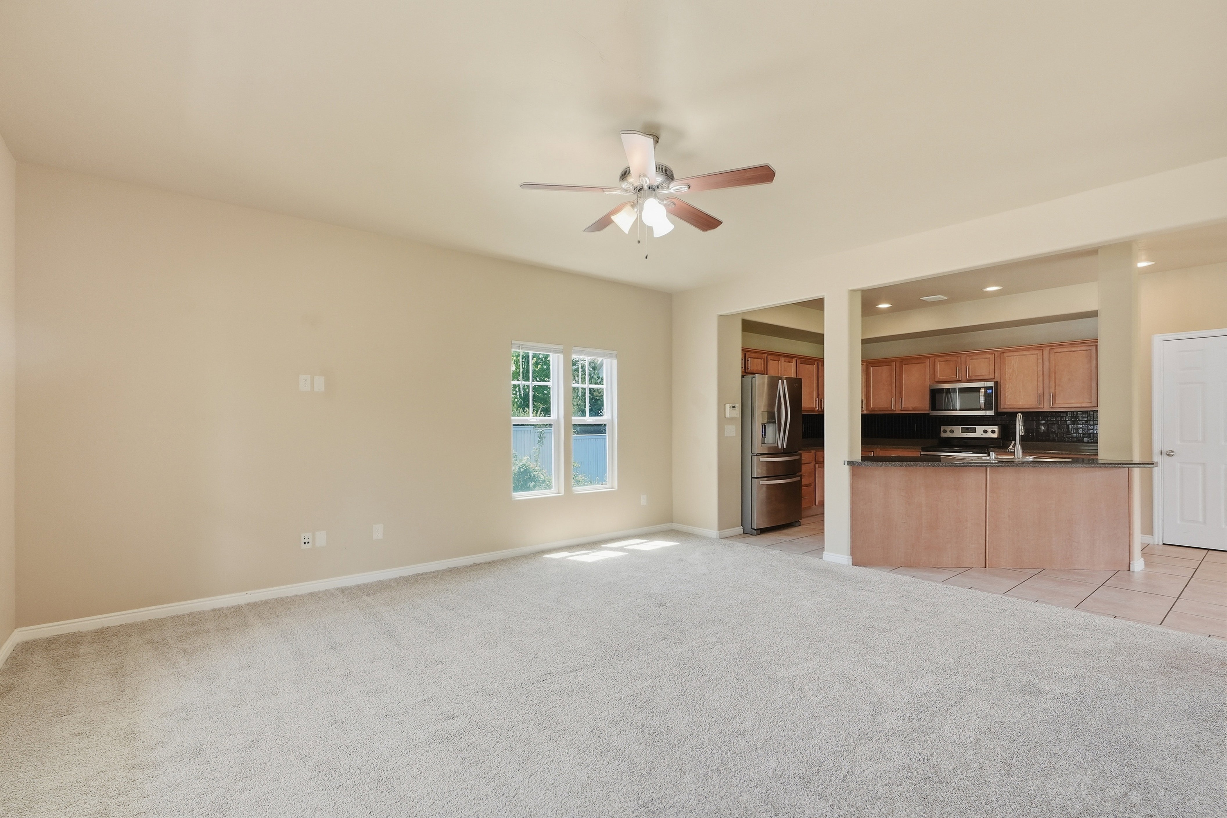 Spacious living area featuring light-colored carpeting and a ceiling fan