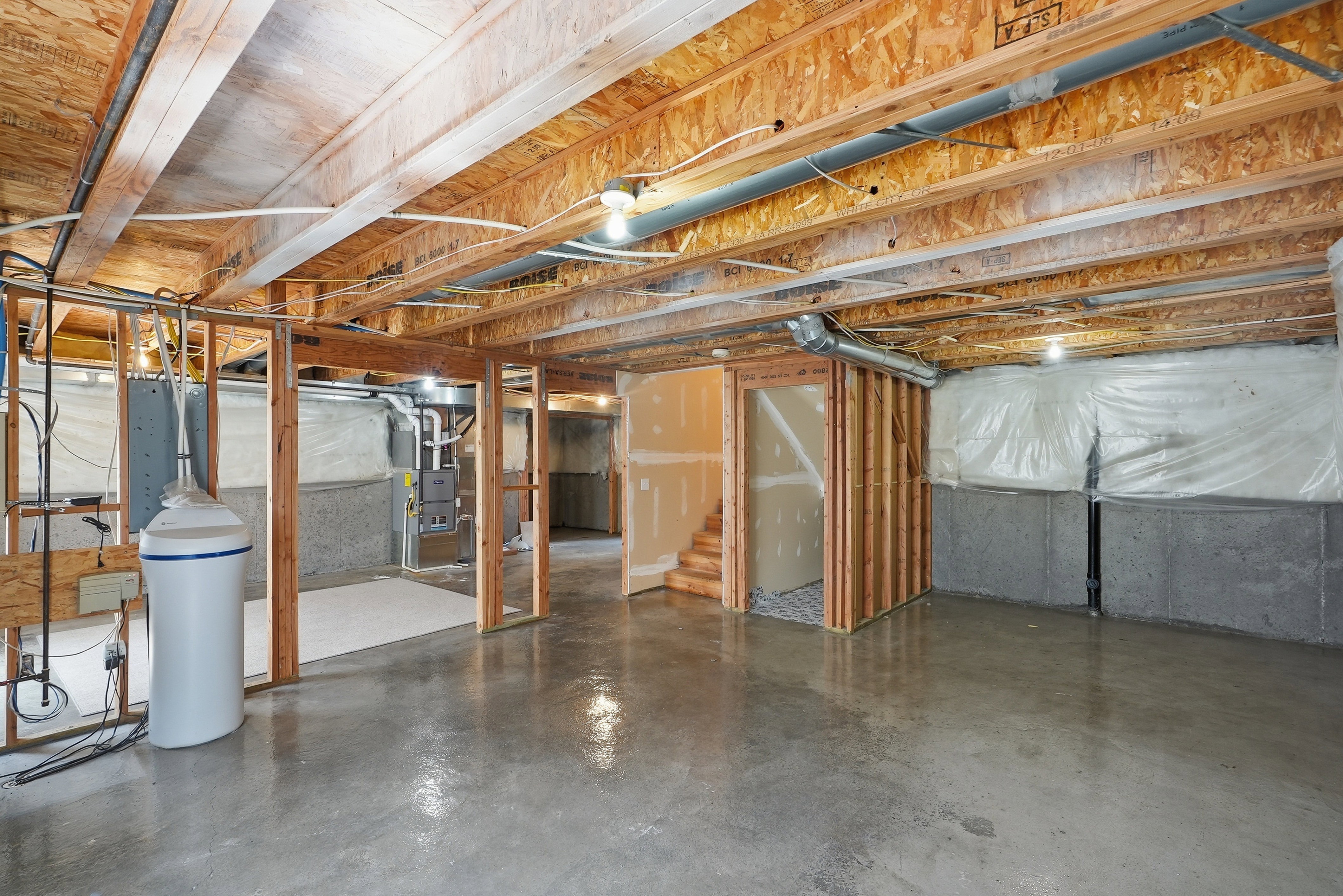 Unfinished basement featuring exposed wood joists, concrete flooring, framed interior walls, and visible utility connections