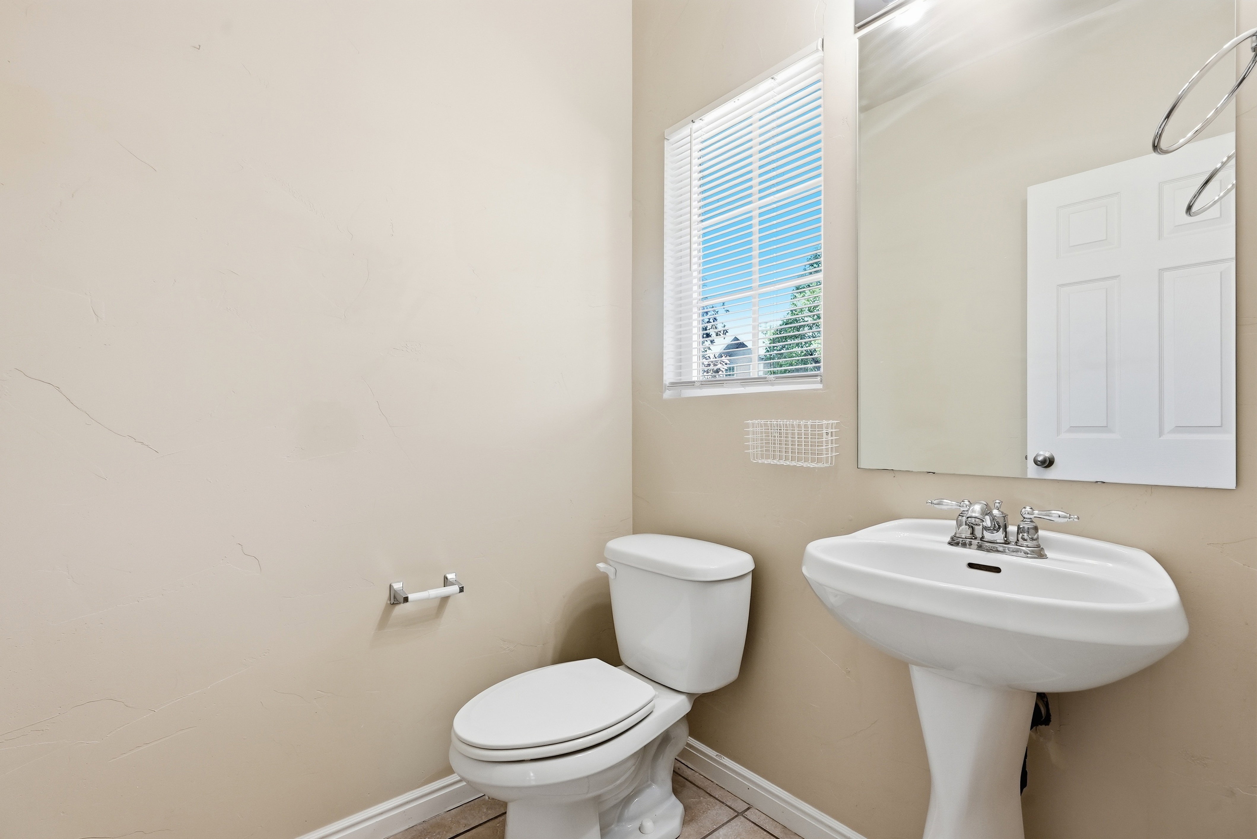 Pedestal sink with chrome faucet, a toilet, and a window with blinds