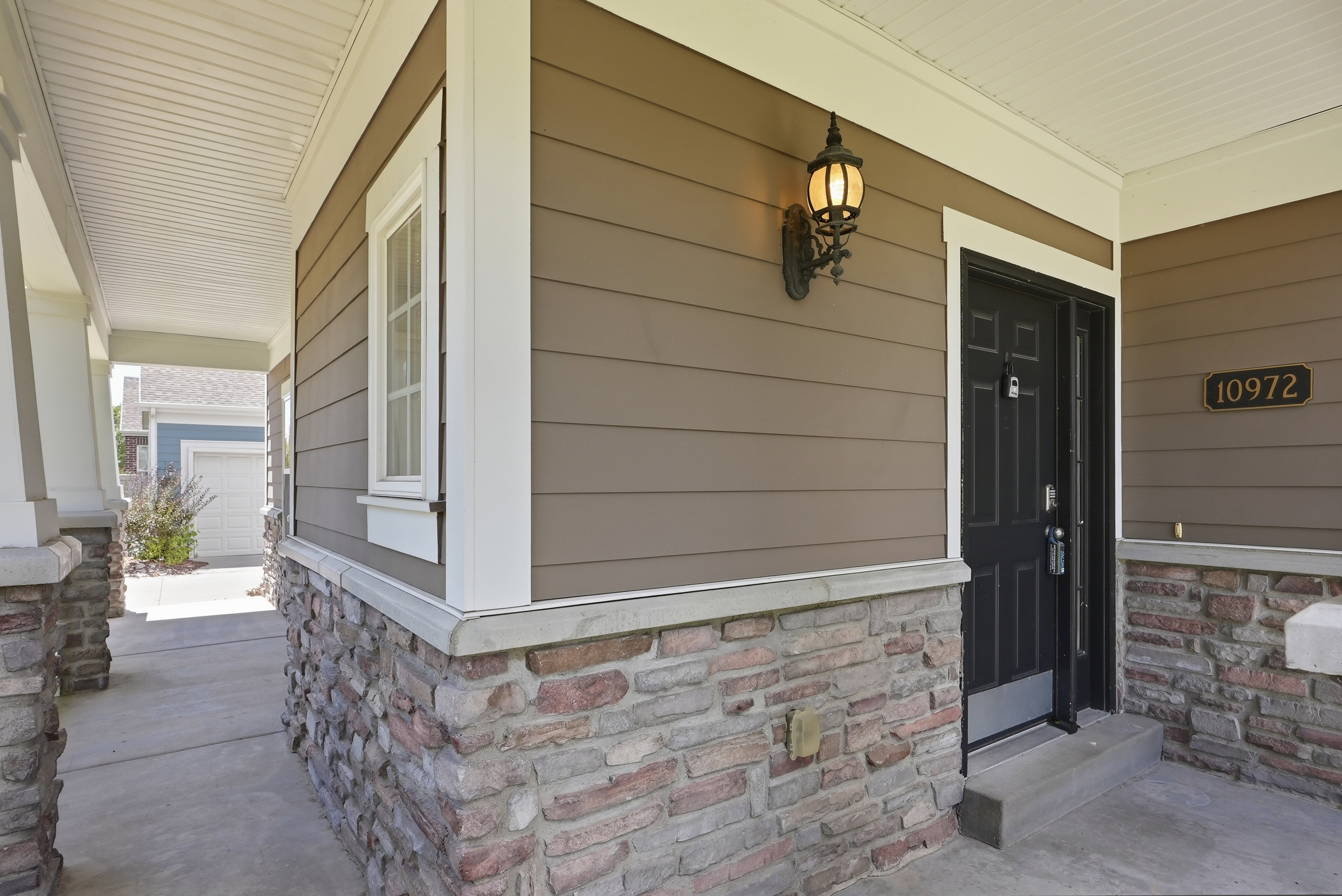 Covered entry featuring stacked stone accents, horizontal siding, a black paneled door, and an exterior wall light fixture