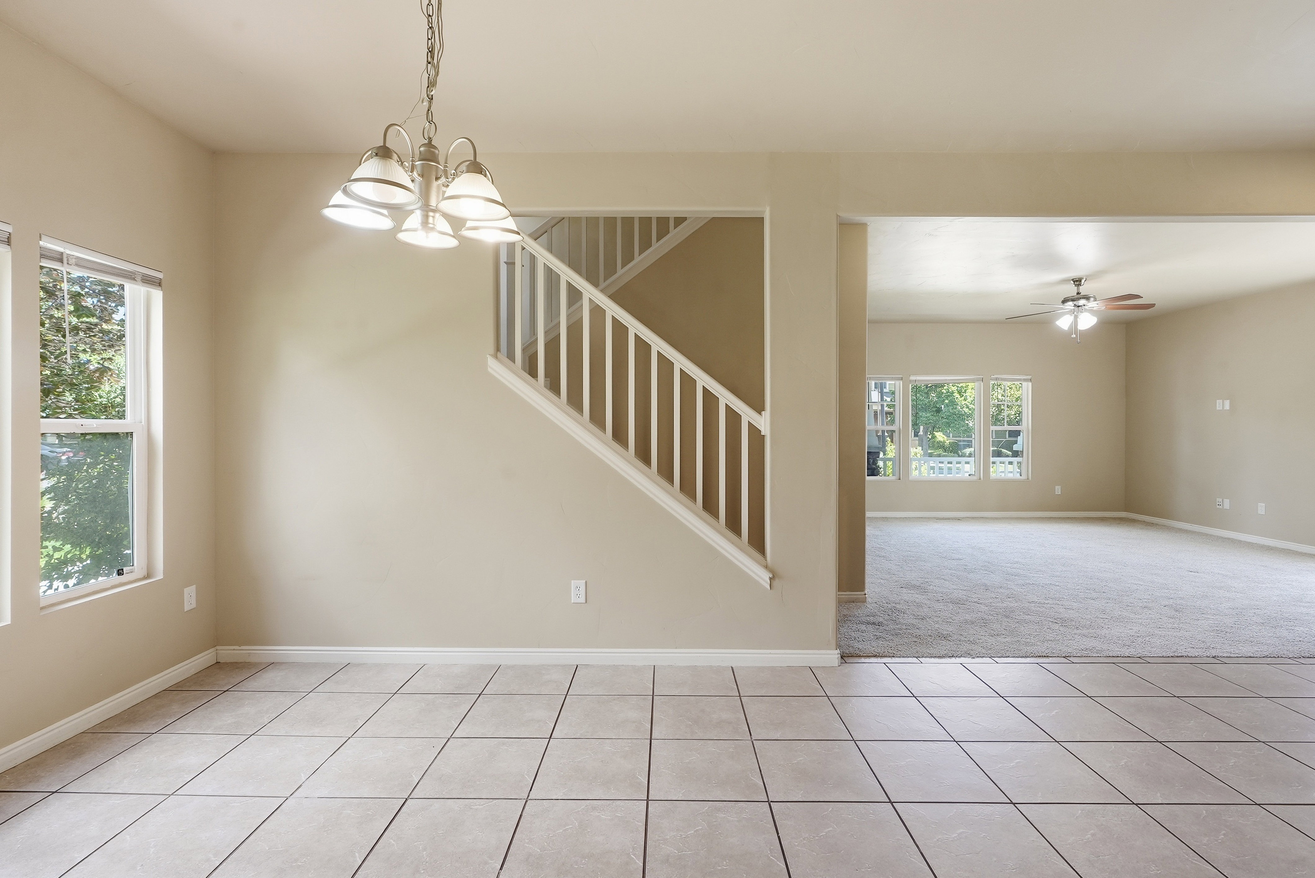 Open-concept interior featuring tile flooring, a chandelier, and a carpeted room with multiple windows and a ceiling fan