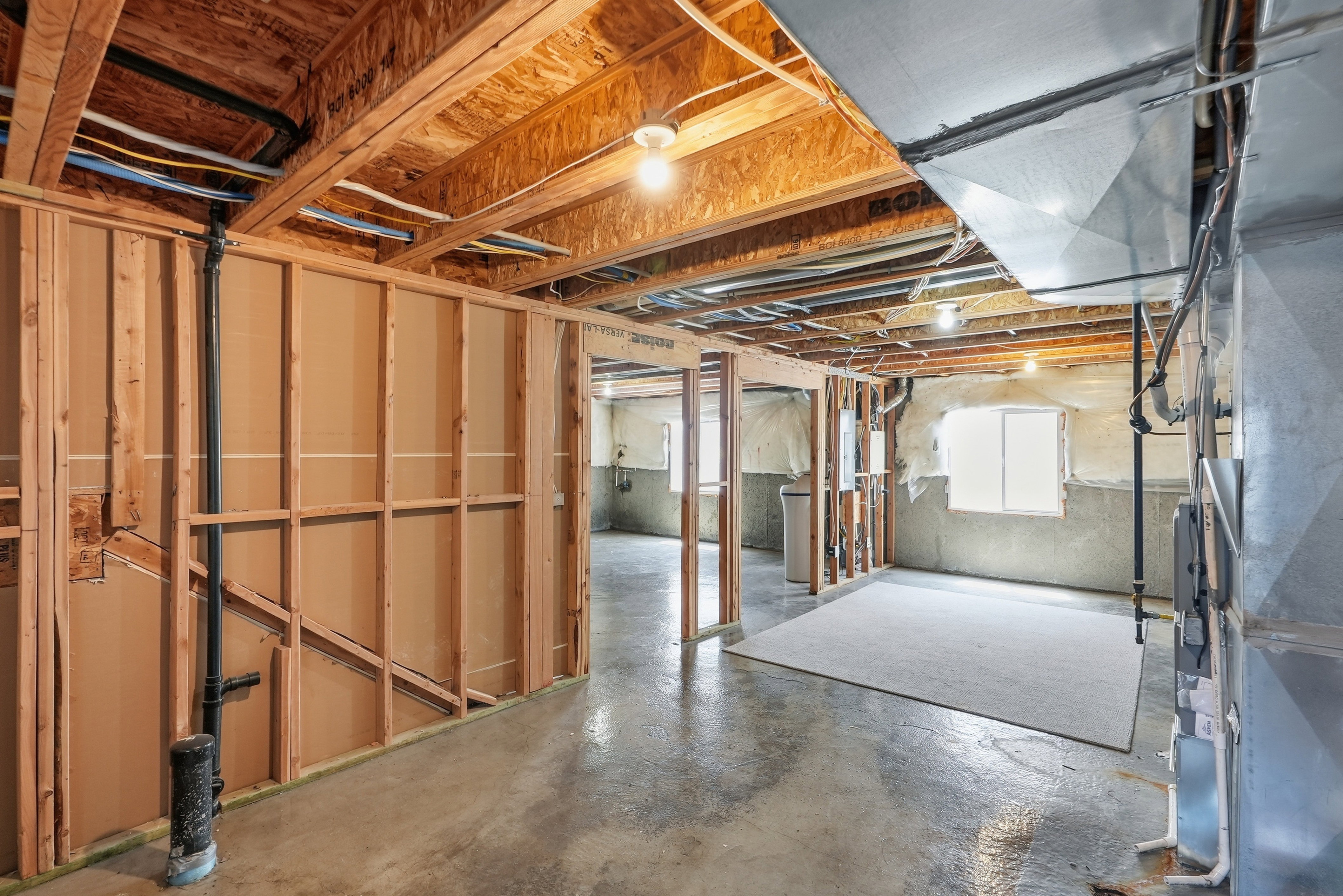 Unfinished basement featuring exposed wood framing, concrete flooring, exposed ceiling joists, and a partial sheetrock wall