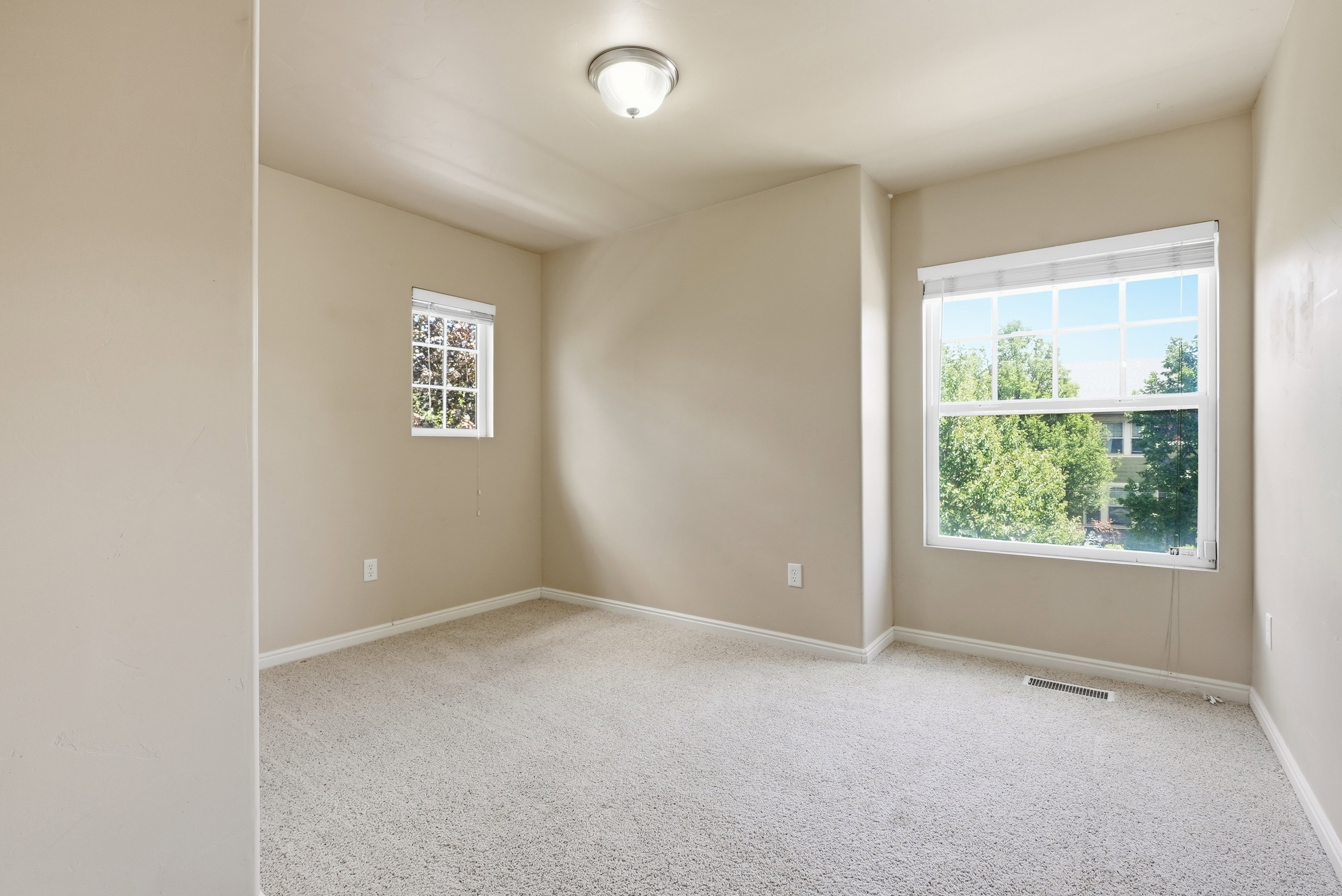 Carpeted room with neutral-toned walls, featuring a large window with white blinds and a smaller secondary window