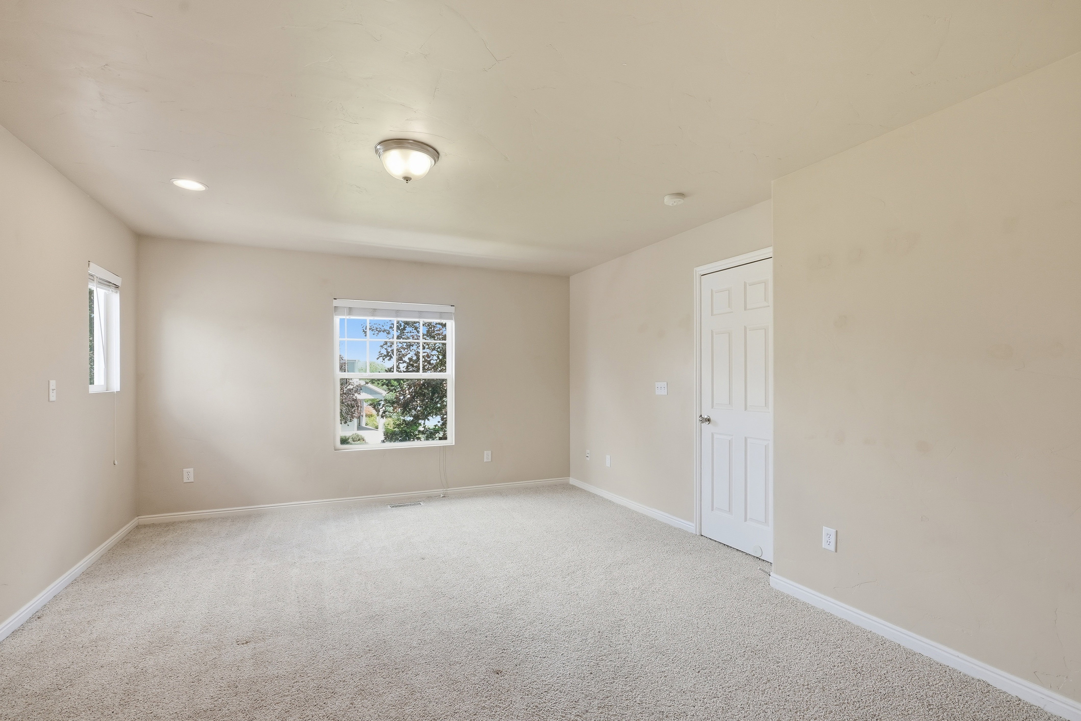 Spacious room featuring carpet flooring, two windows with blinds, a paneled interior door, recessed lighting, and a semi-flush mount ceiling fixture