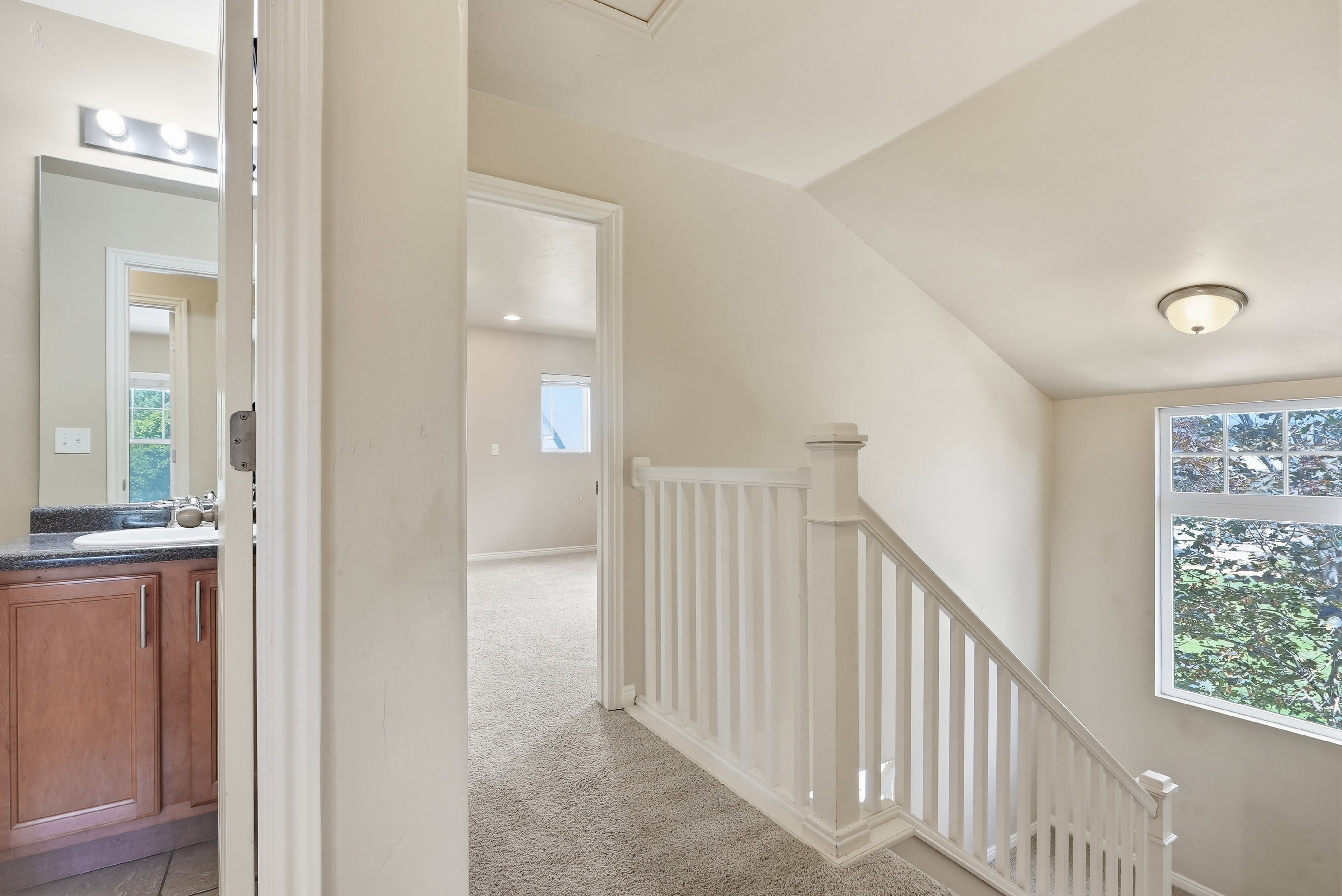 Carpeted hallway and staircase featuring a white painted banister and natural light from a window