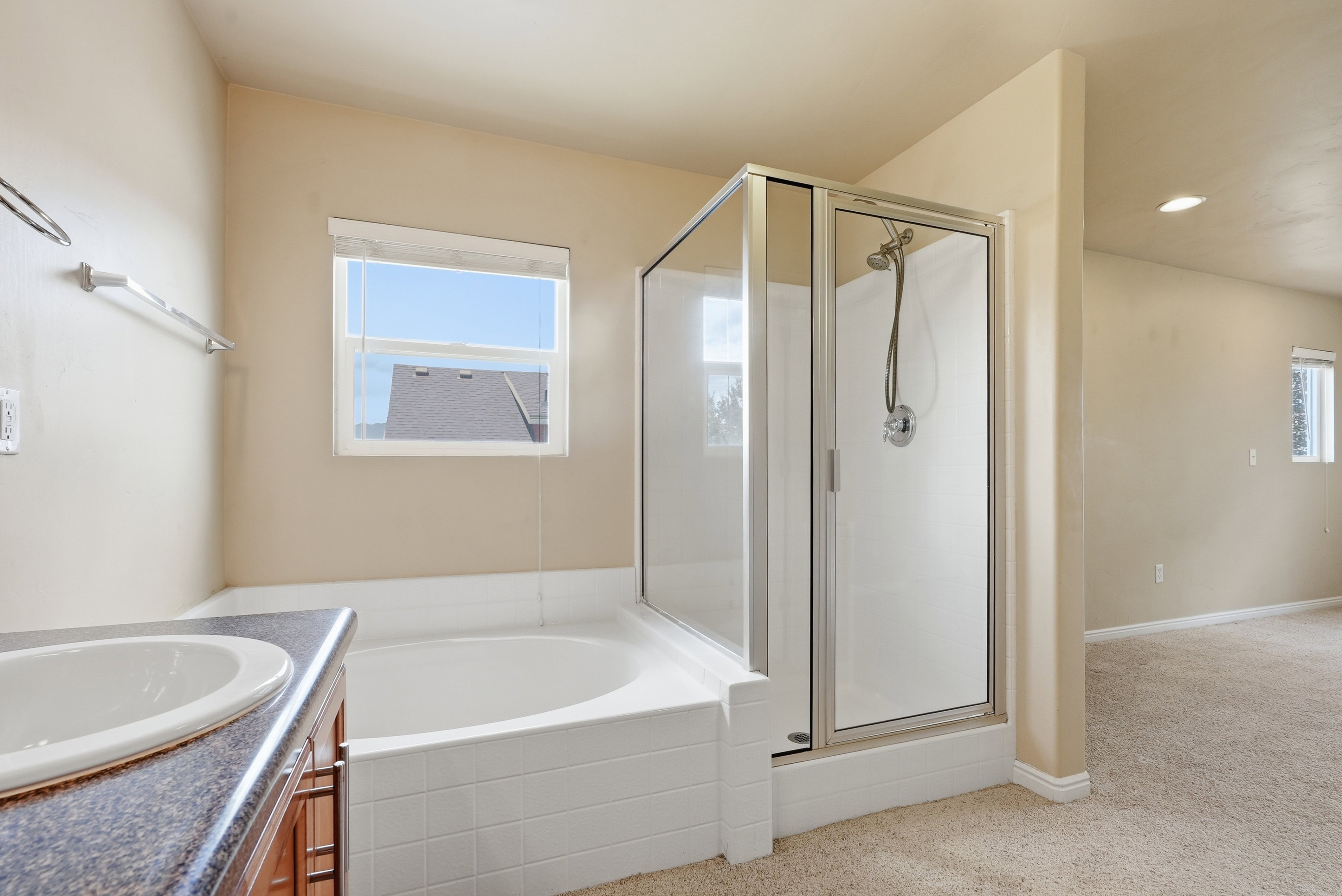 Bathroom featuring a built-in soaking tub, a separate glass-enclosed shower, a vanity with an integrated sink, a dark countertop, and warm-toned cabinetry