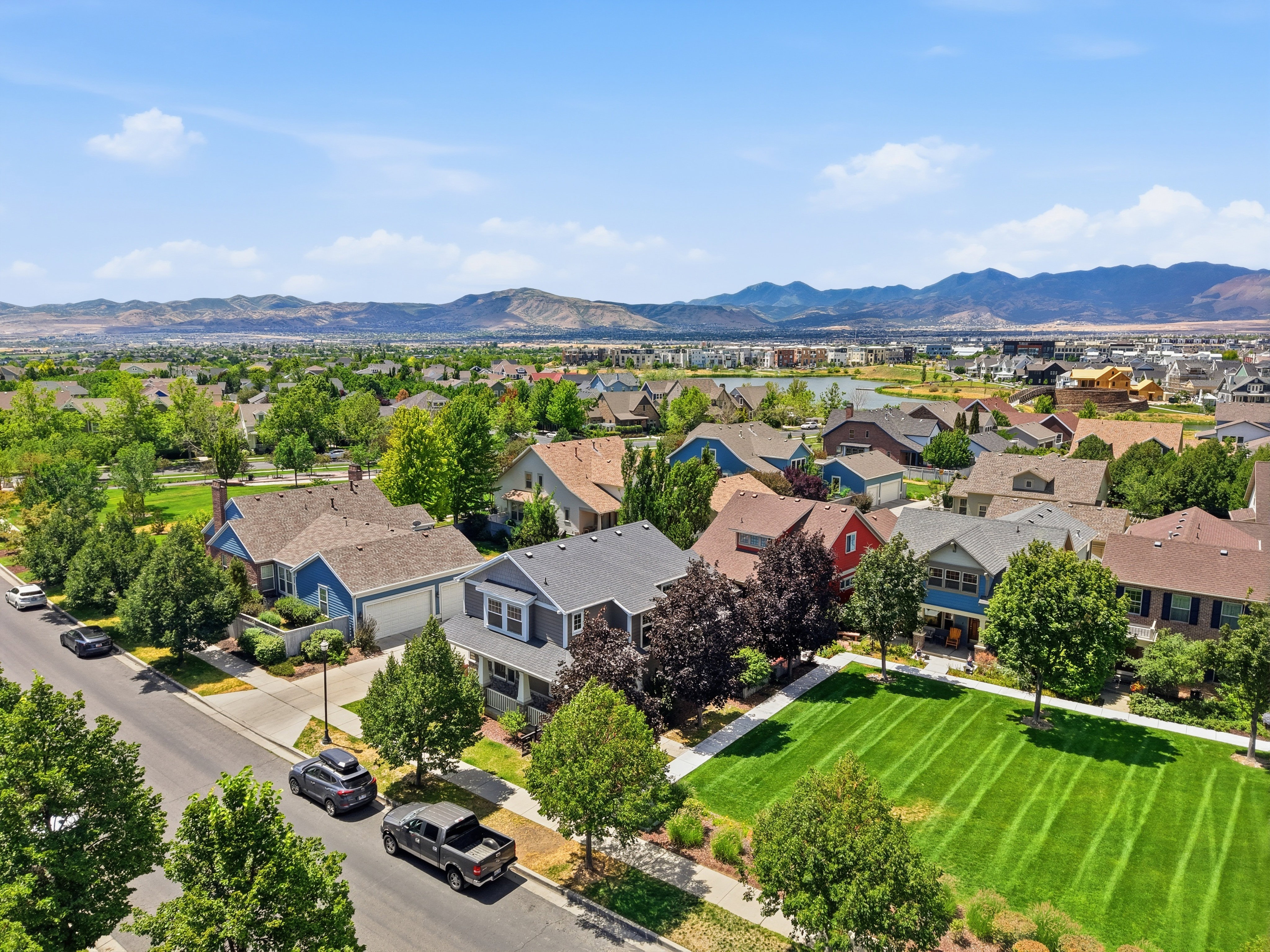 Residential street with mature trees and maintained lawns, mountains in the distance, and a body of water