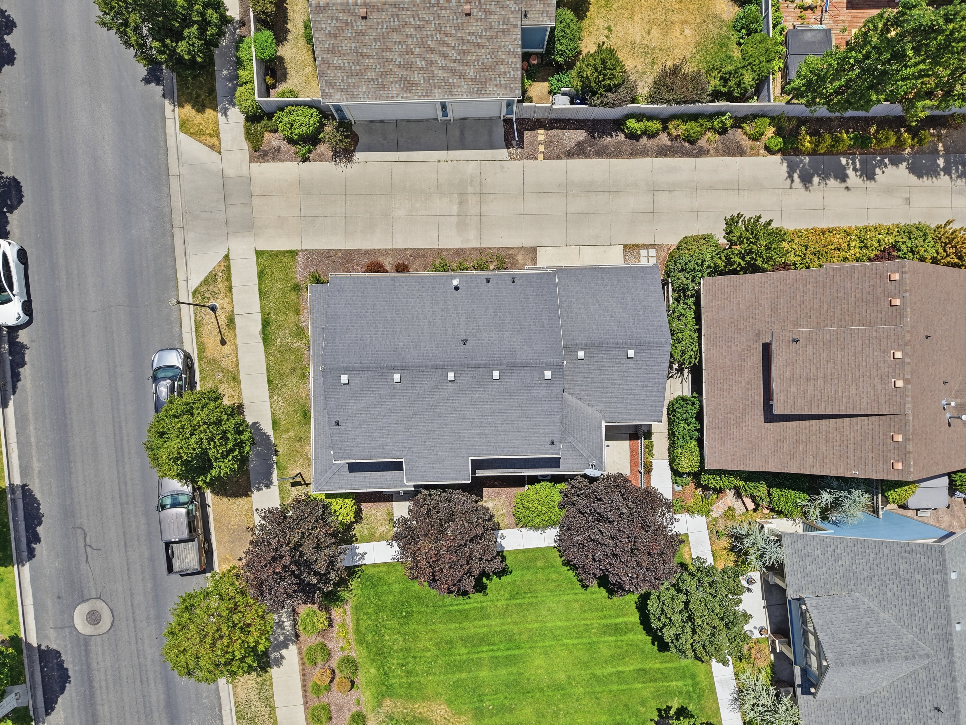 Property with a dark gray shingle roof, green lawn, and mature trees