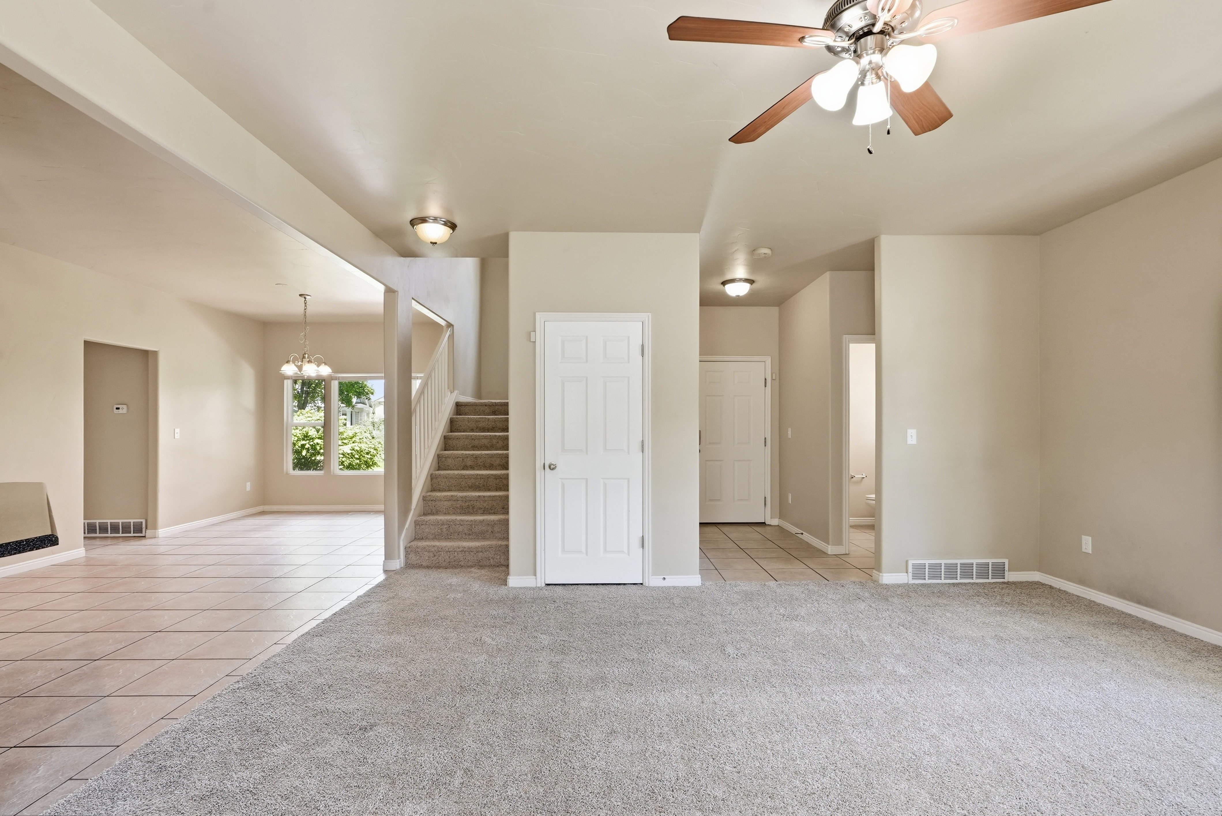 Open-concept interior featuring a ceiling fan with integrated lighting, a carpeted living area, and a tiled dining area with outdoor views