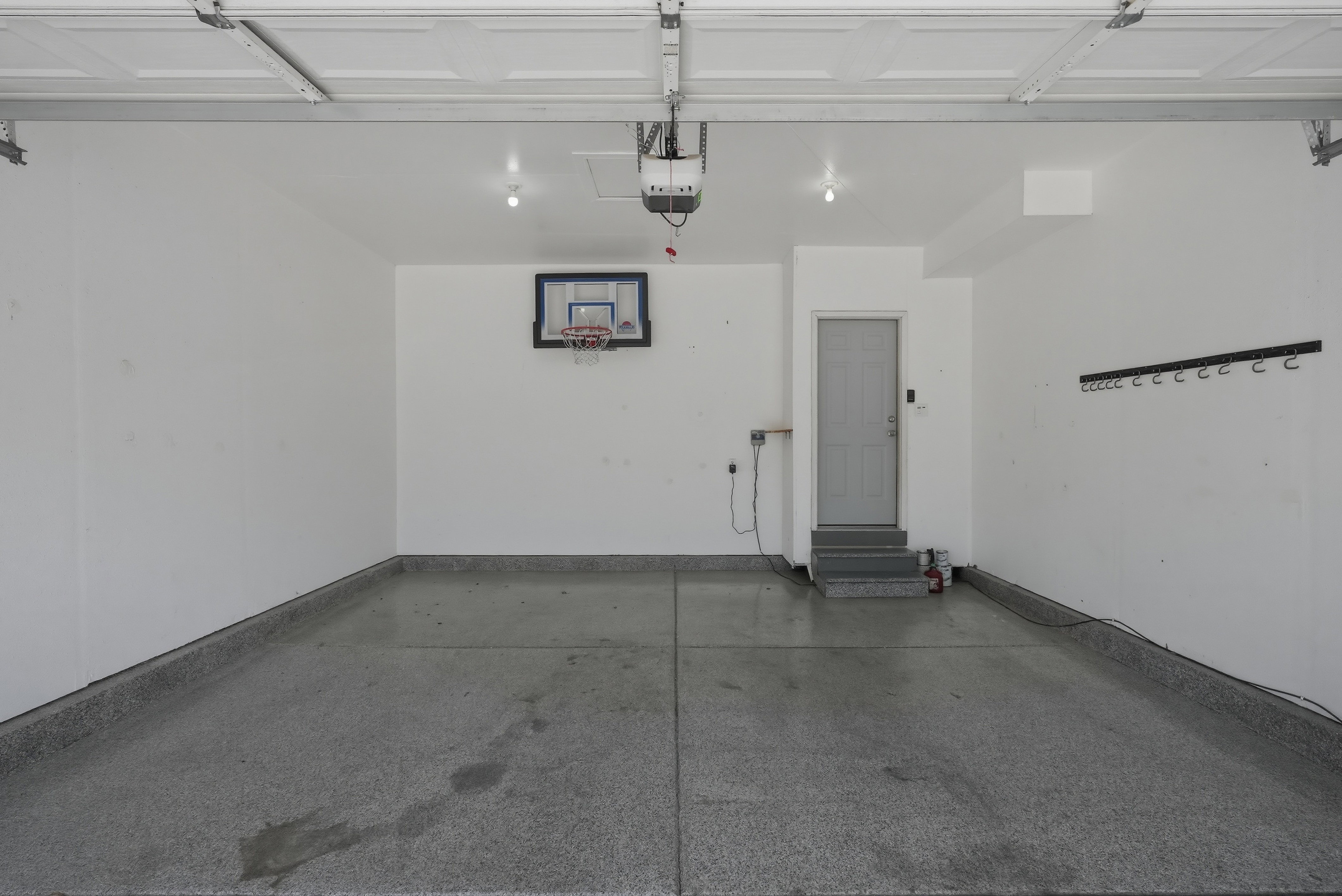 Spacious garage featuring a durable epoxy-coated floor, overhead door, interior access door, wall-mounted storage hooks, and ceiling-mounted lighting fixtures