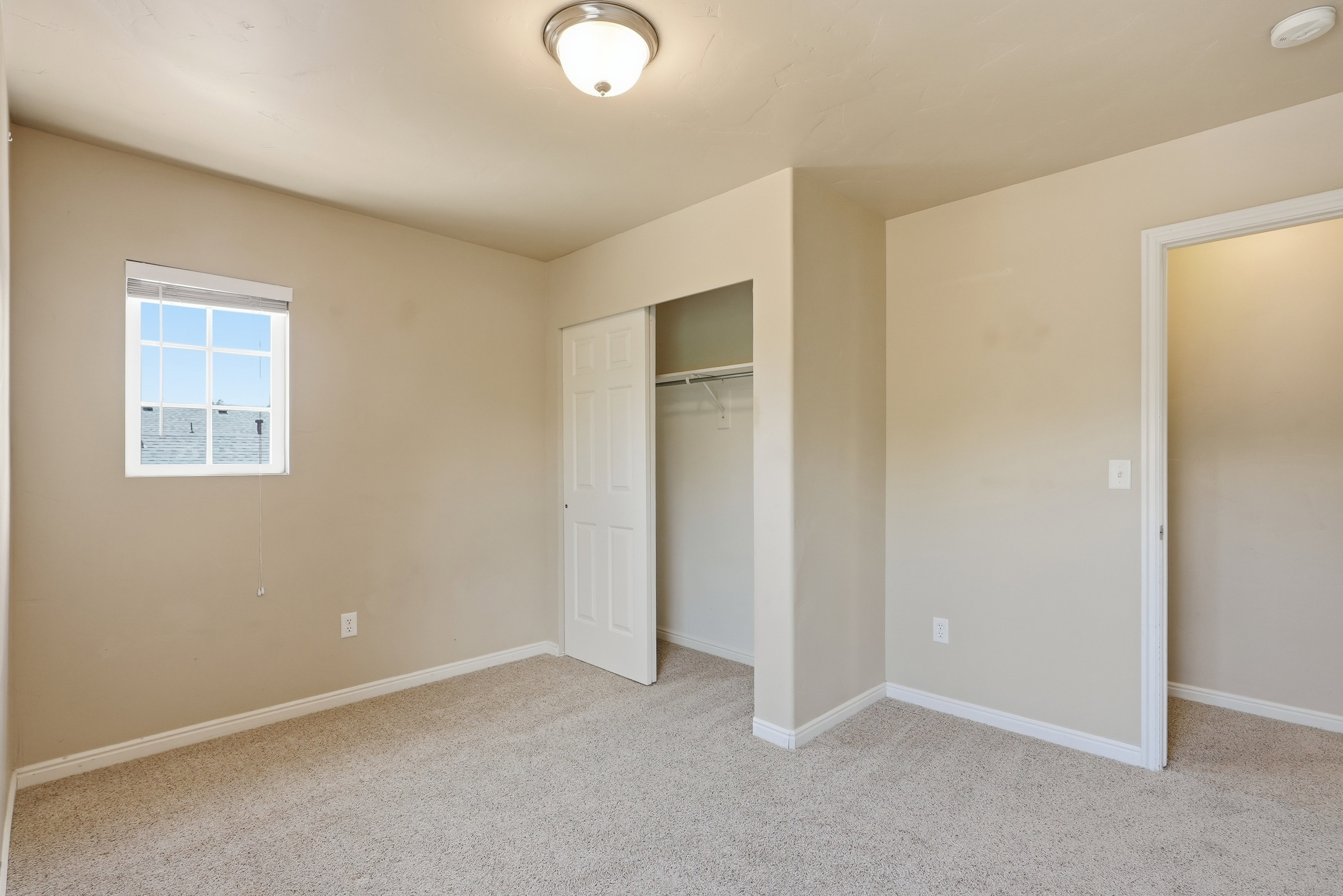 Bedroom featuring light neutral paint, wall-to-wall carpeting, a window with blinds, and a bi-fold closet