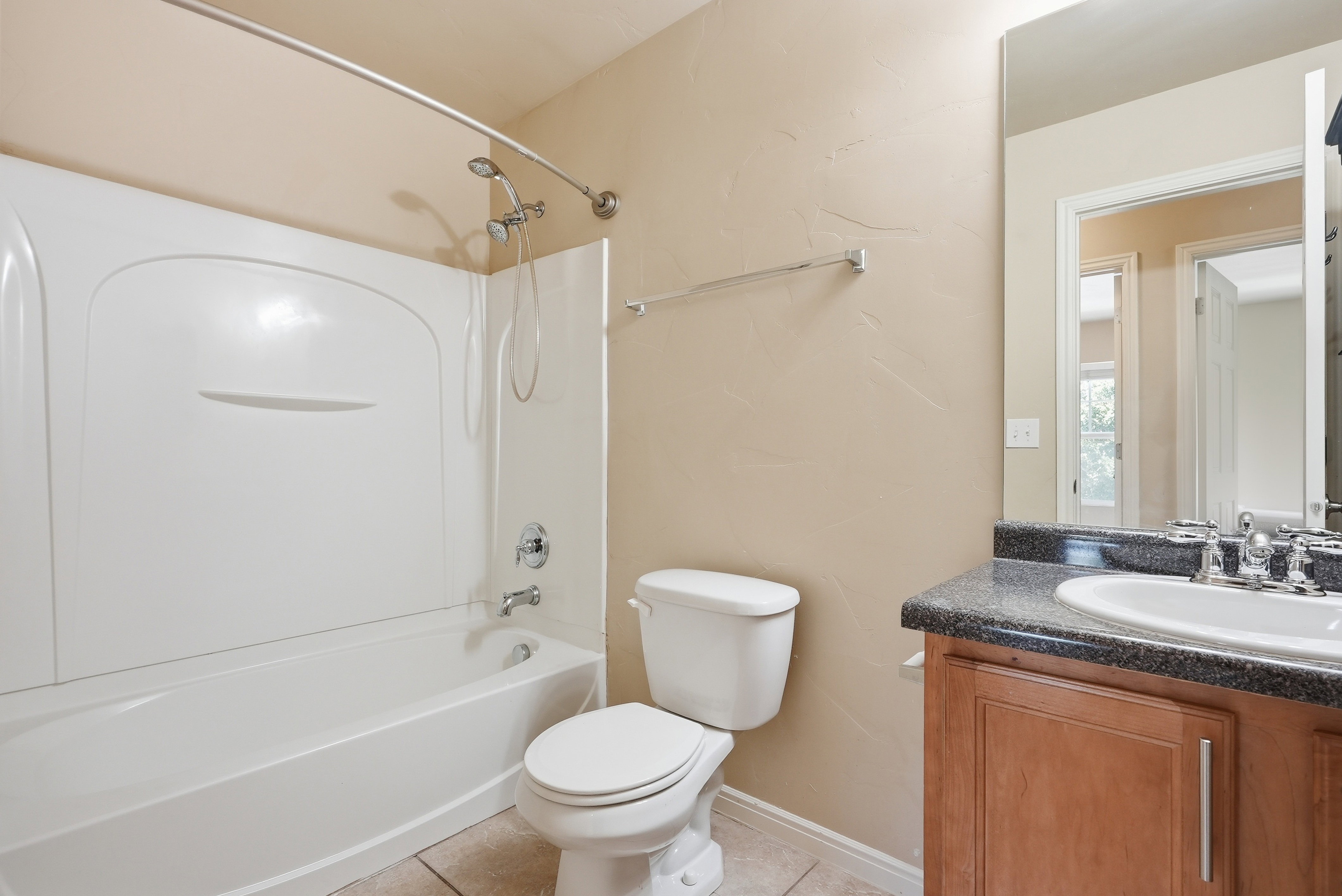 Bathroom featuring a shower-tub combination with a curved shower rod, a single vanity with a dark countertop, an undermount sink, and neutral wall paint