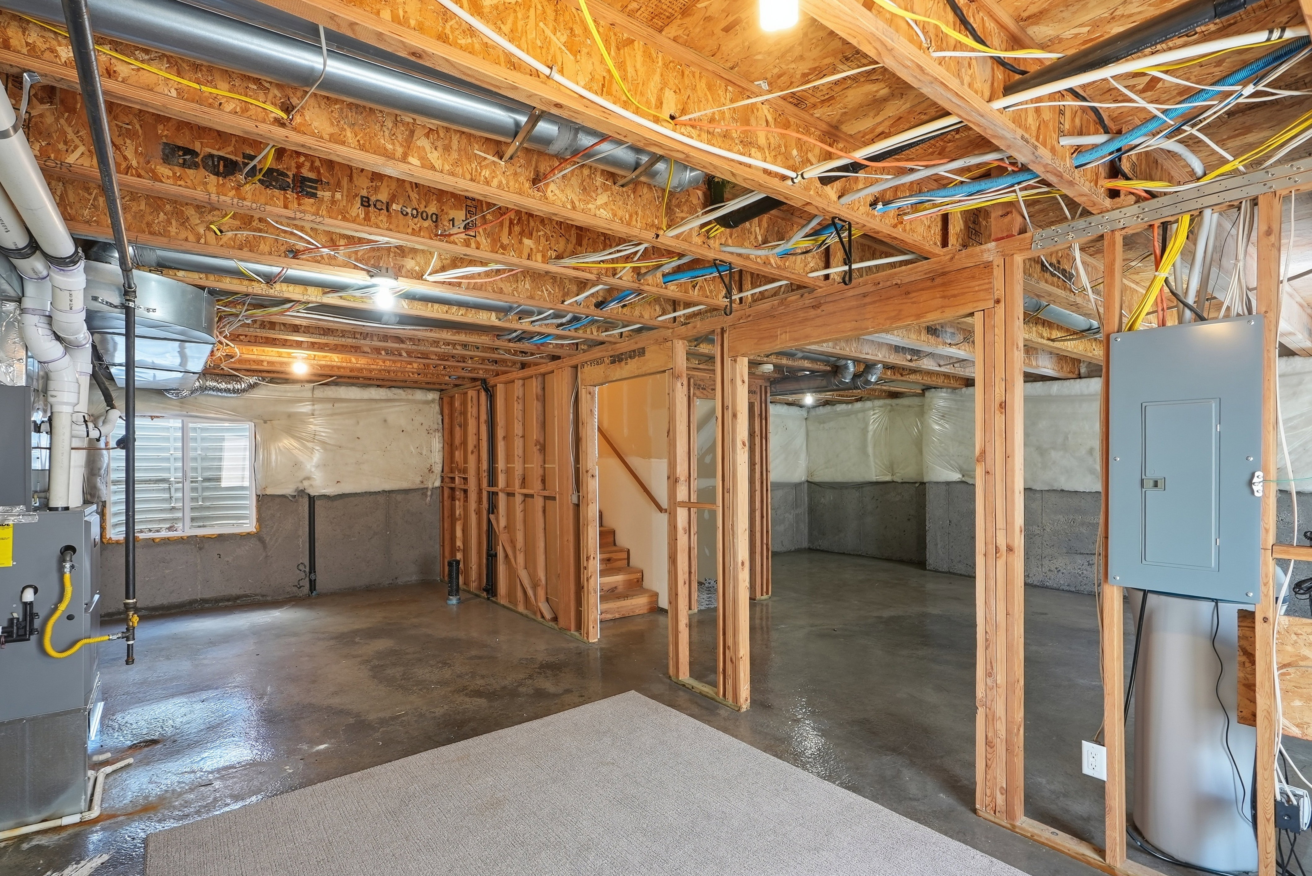 Unfinished basement presenting wood framing, exposed joists, concrete flooring, and an electrical panel